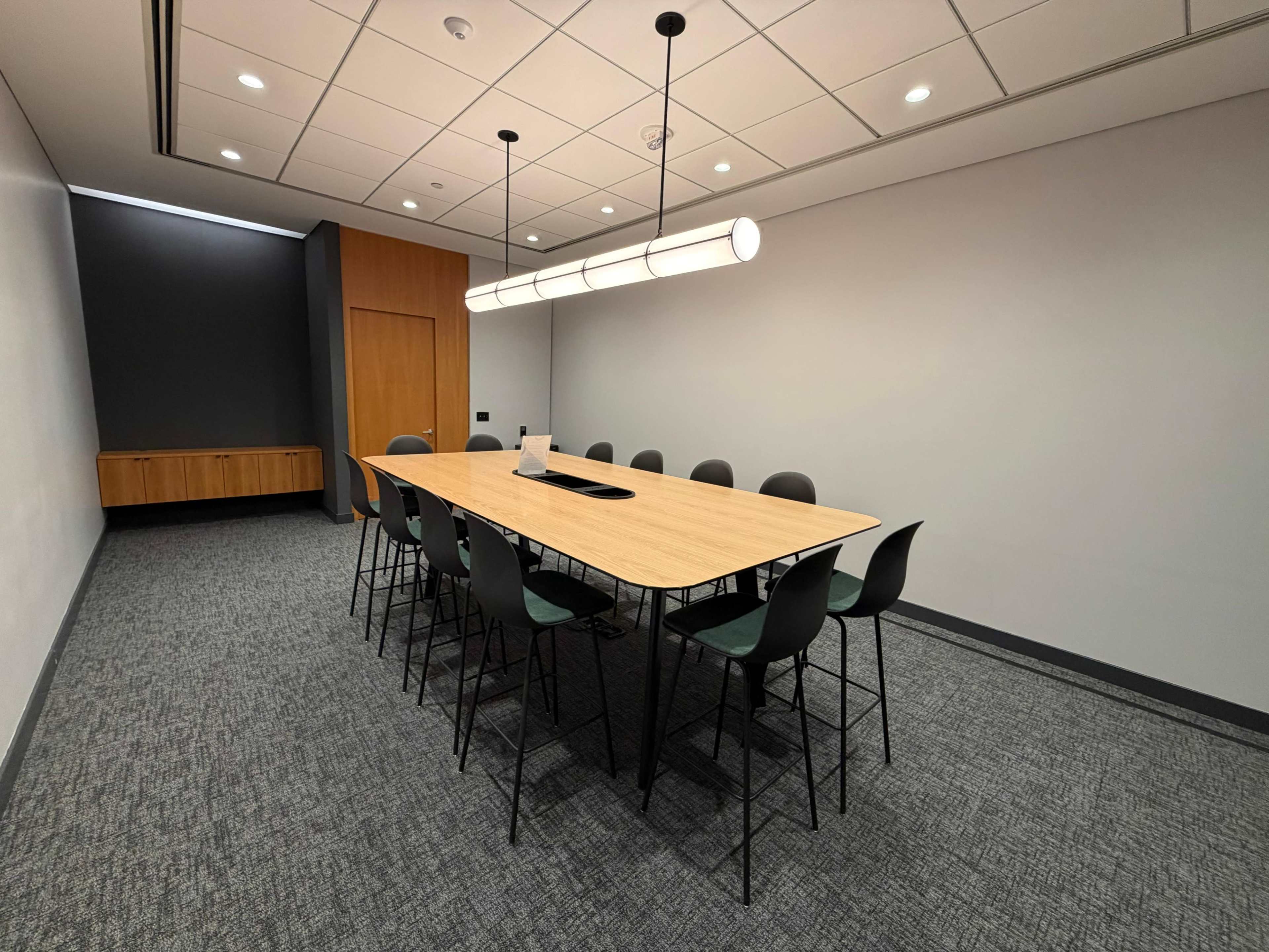 The image shows a modern conference room with a long wooden table, black chairs, and a minimalist design.