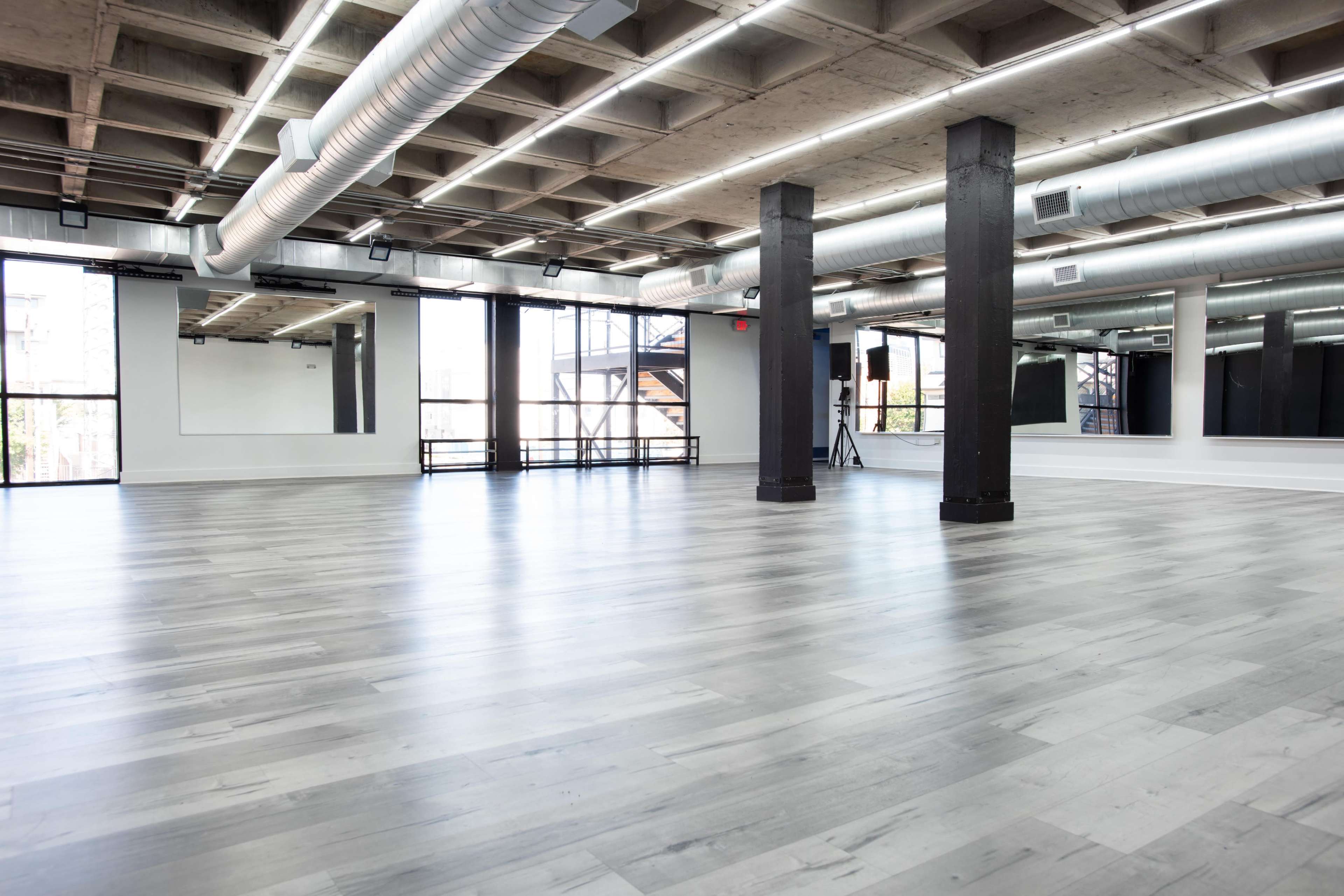 A spacious, modern studio with large windows, polished wooden floors, and exposed ductwork.