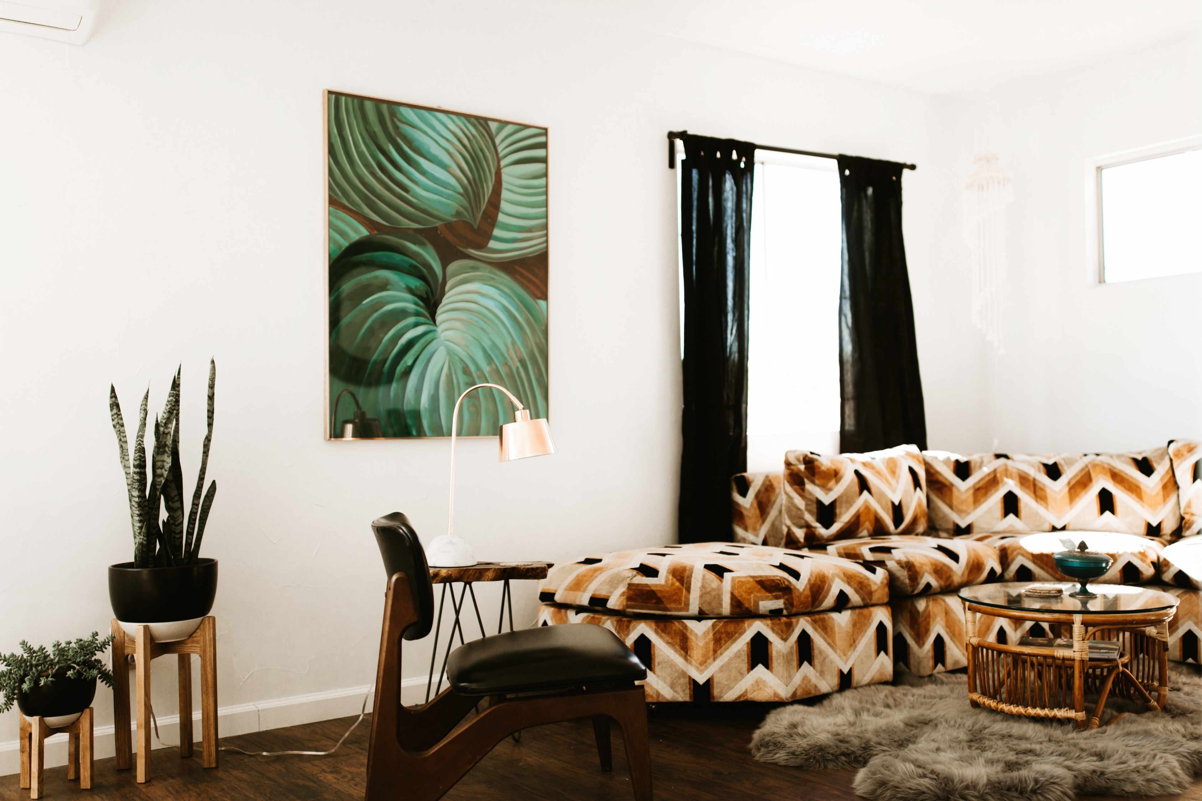 A modern living room features a patterned sectional sofa, a plant, a lamp, and artwork depicting green leaves.