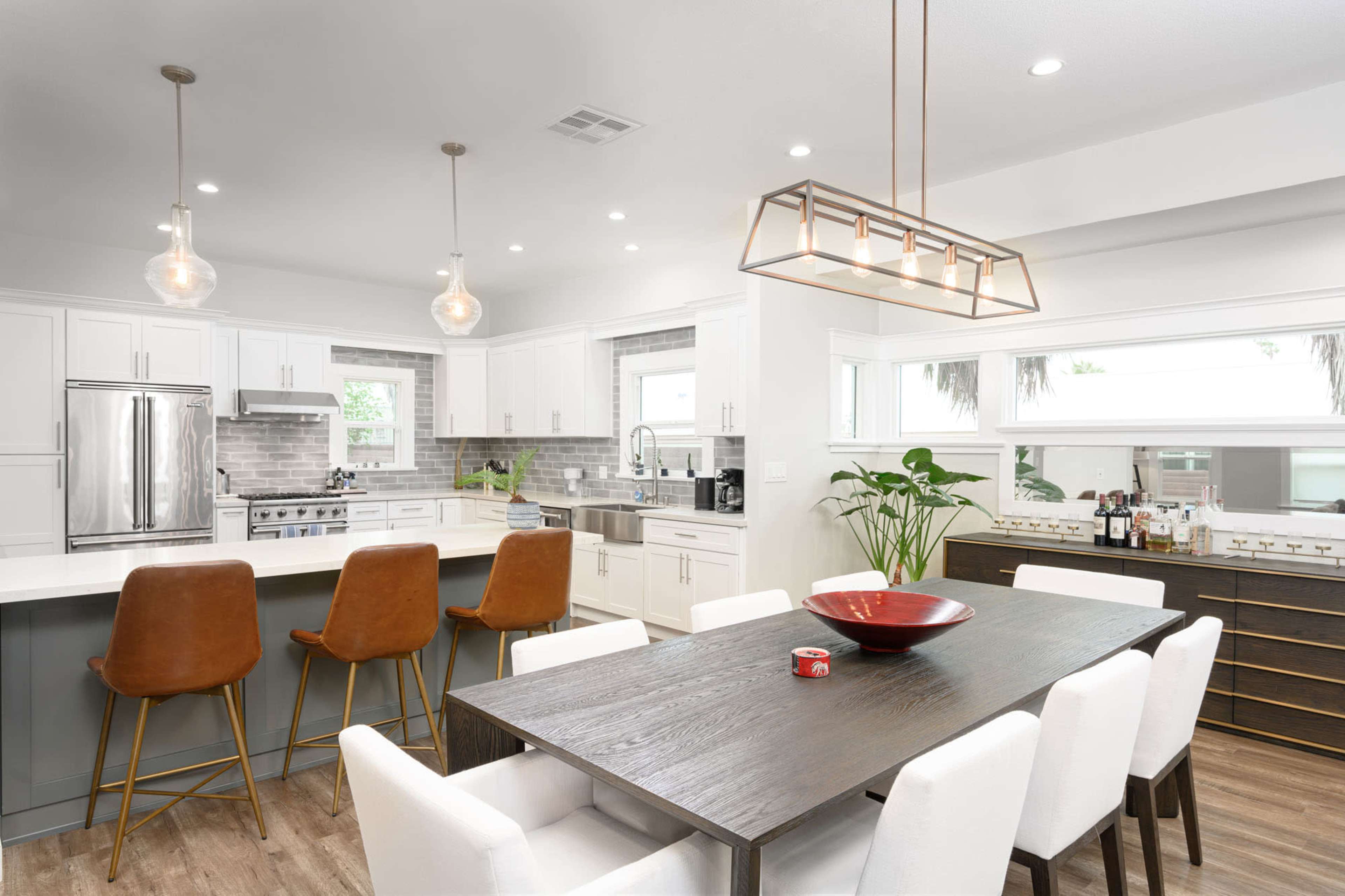 A modern kitchen and dining area with a large wooden dining table, white upholstered chairs, and sleek cabinetry.