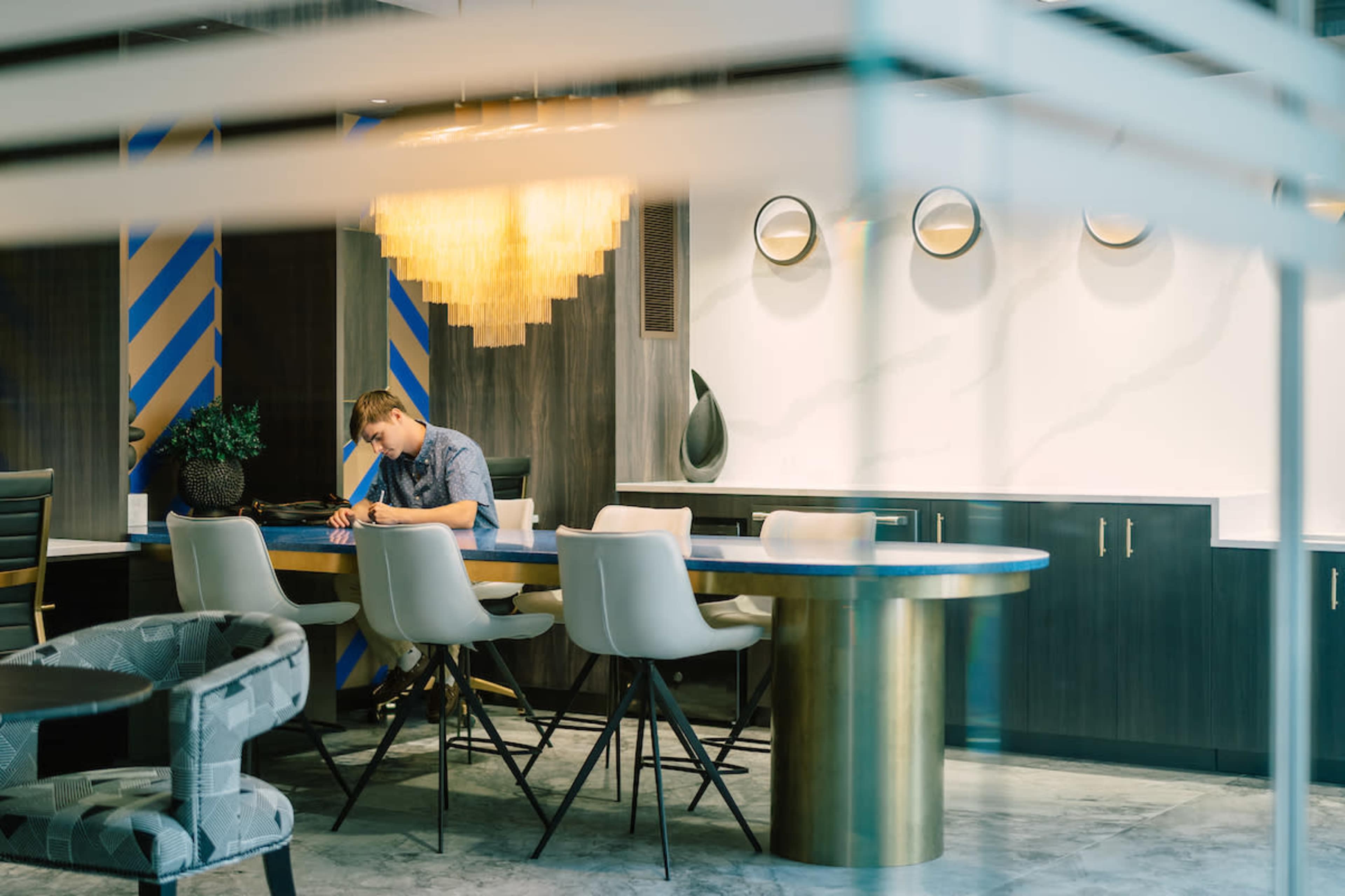 A man sits alone at a modern round table in a well-lit dining area with stylish furnishings and decorative wall accents.