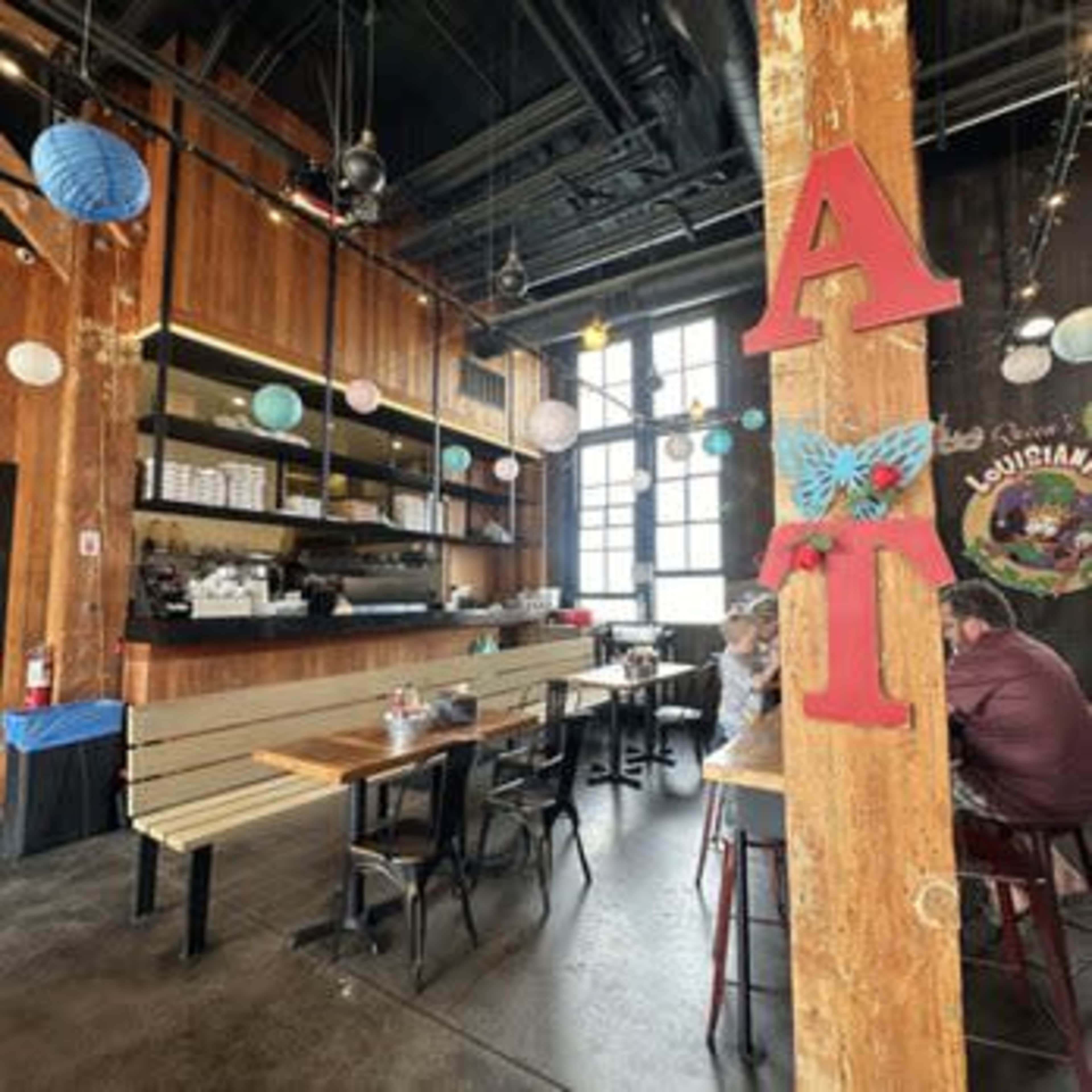 The image shows the interior of a restaurant featuring wooden panels, tables with black chairs, and colorful hanging lanterns.
