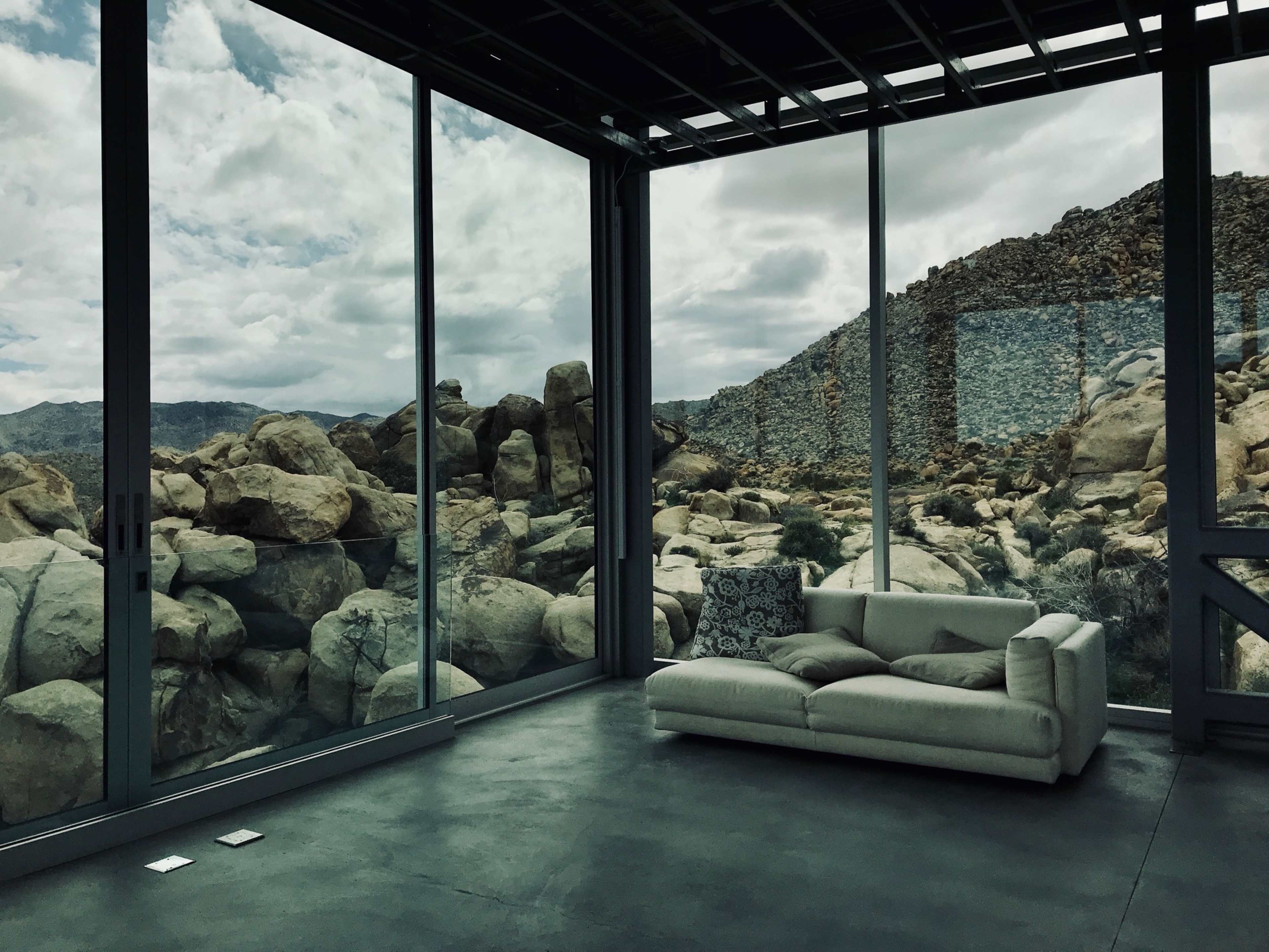 A modern interior with a white couch, large glass windows, and rocky terrain visible outside.