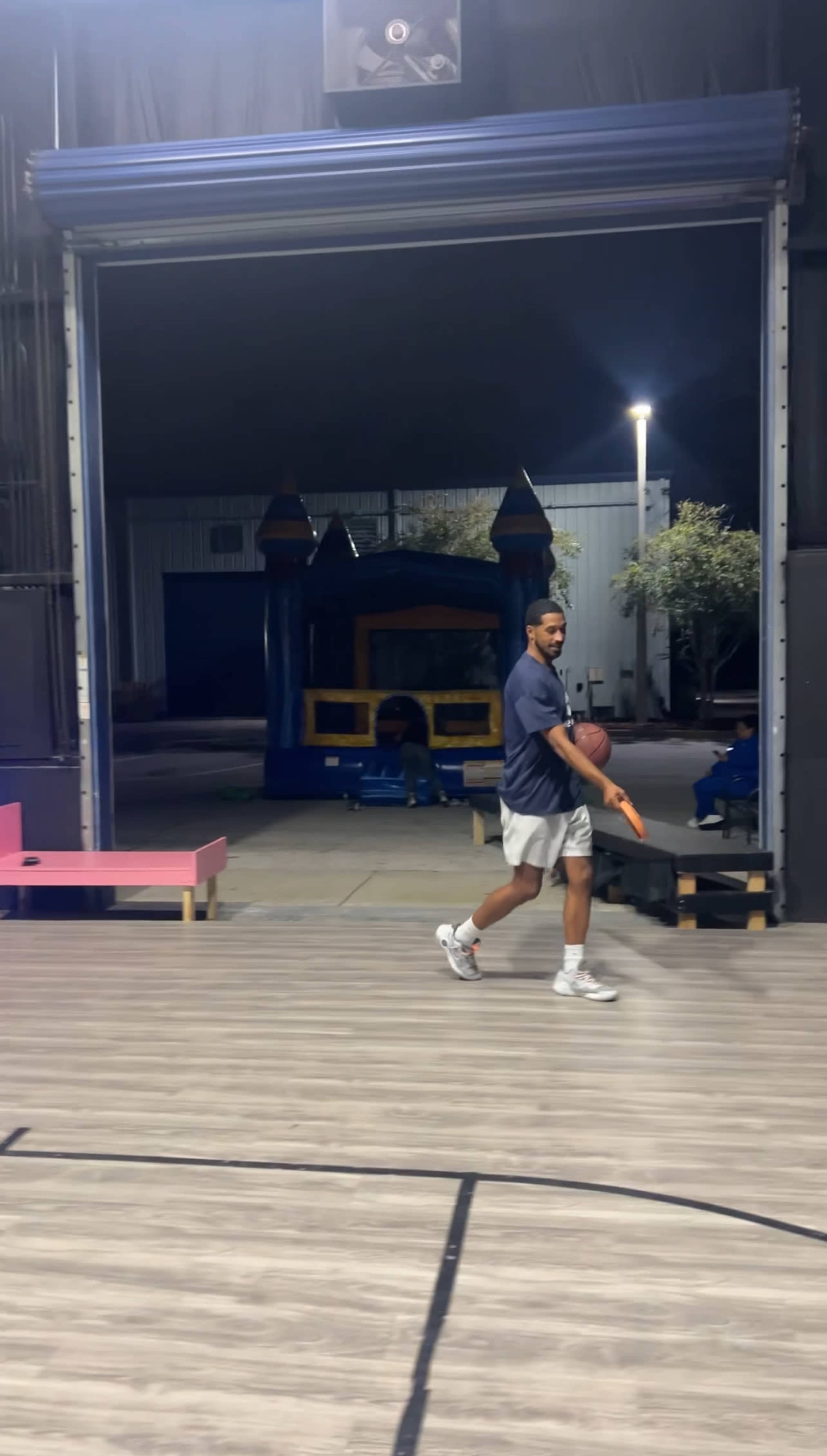 A person walks across a wooden floor near a large inflatable bounce house in an indoor space.