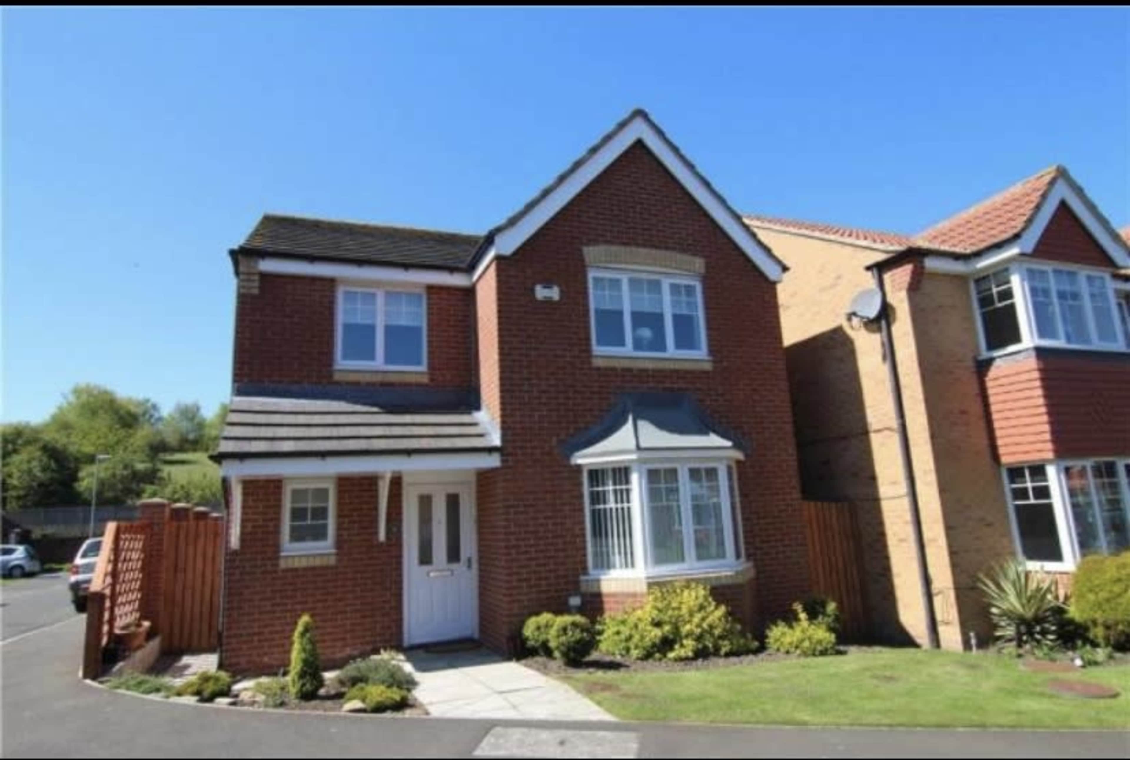 A two-story brick house with a sloped roof, a front porch, and landscaped garden is situated in a residential area.