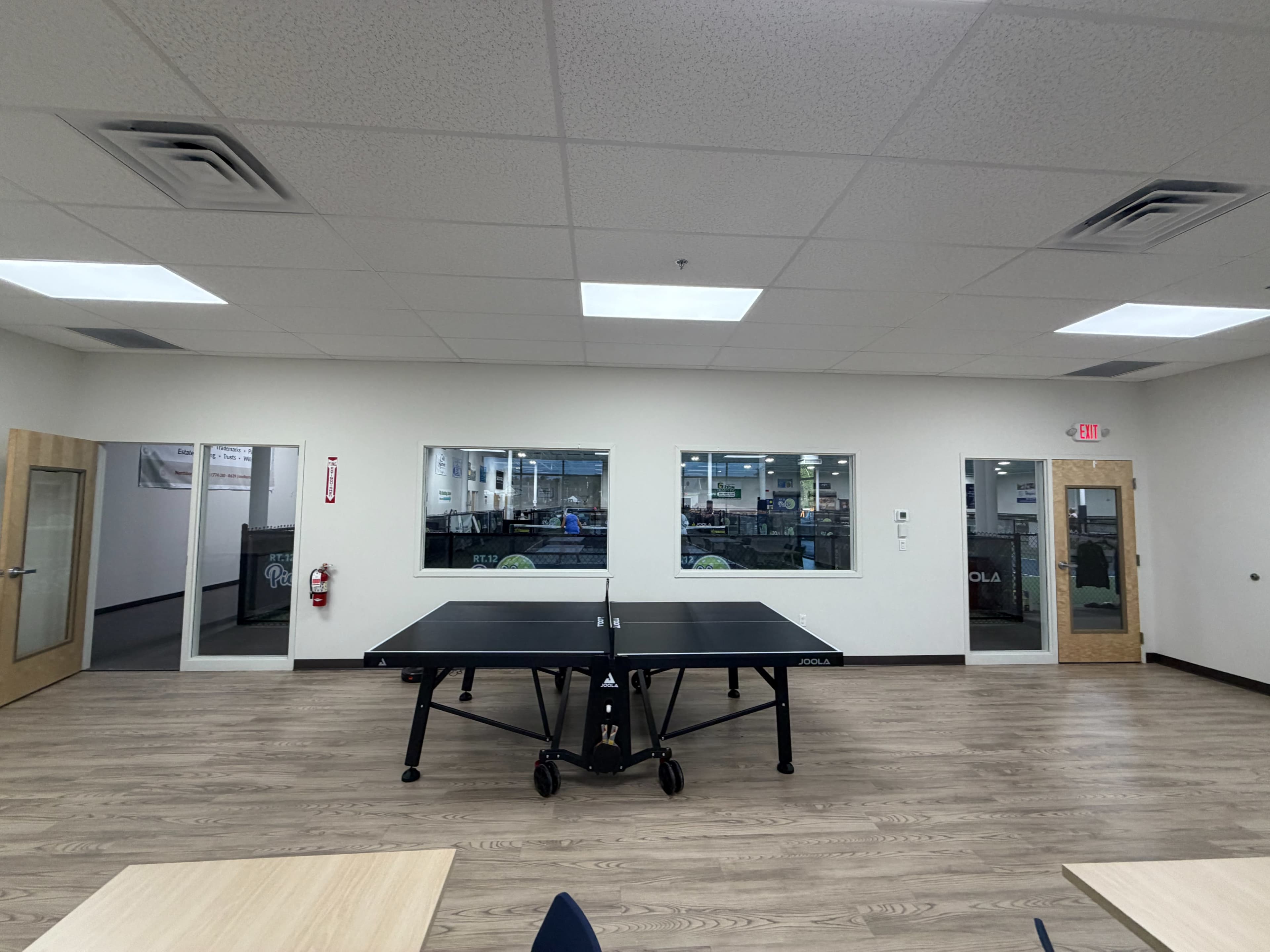 The image shows a spacious room with a table tennis table in the center, surrounded by doors and windows leading to other areas.