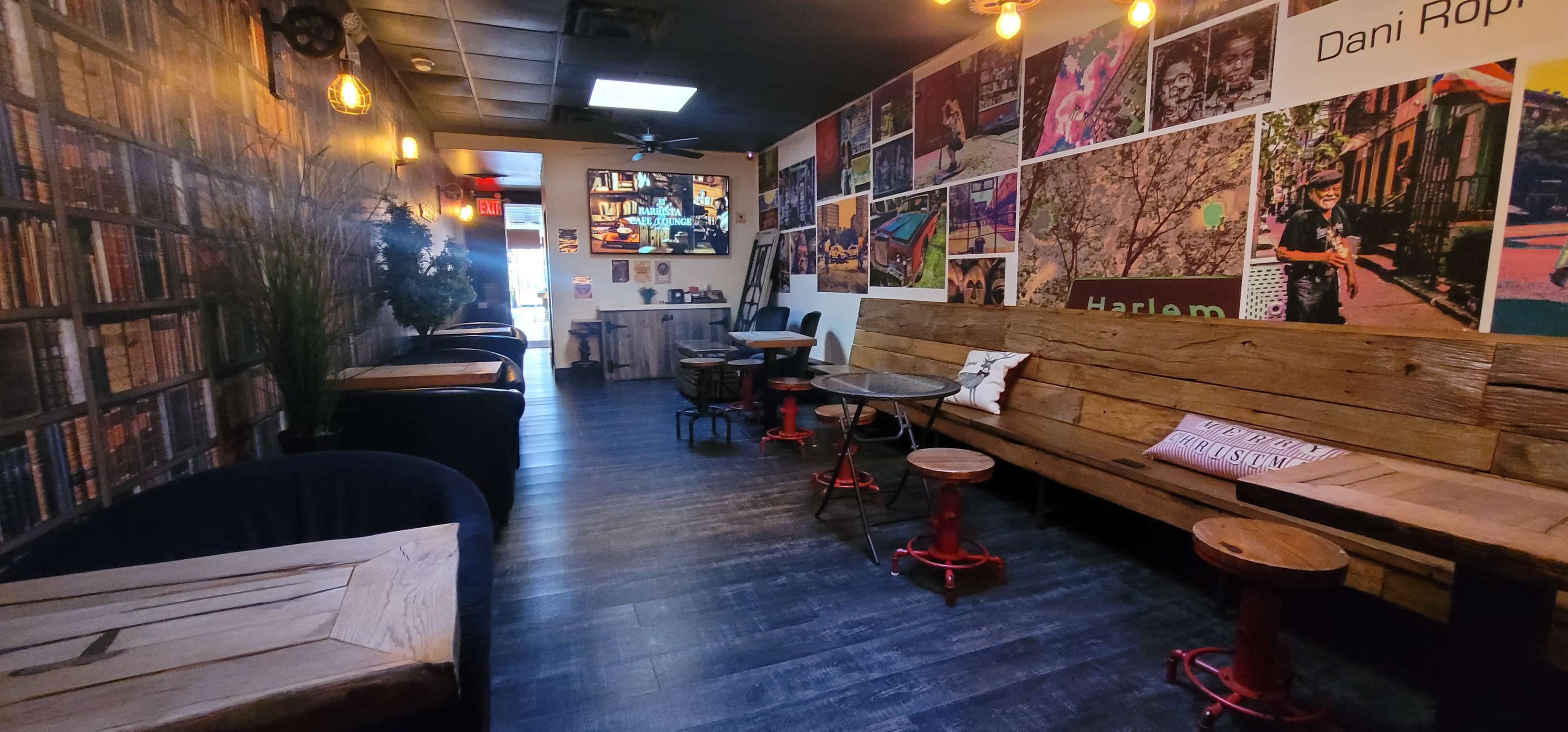 The image shows a cozy café interior with wooden seating, a wall covered in framed photographs, and a few small tables arranged throughout the space.