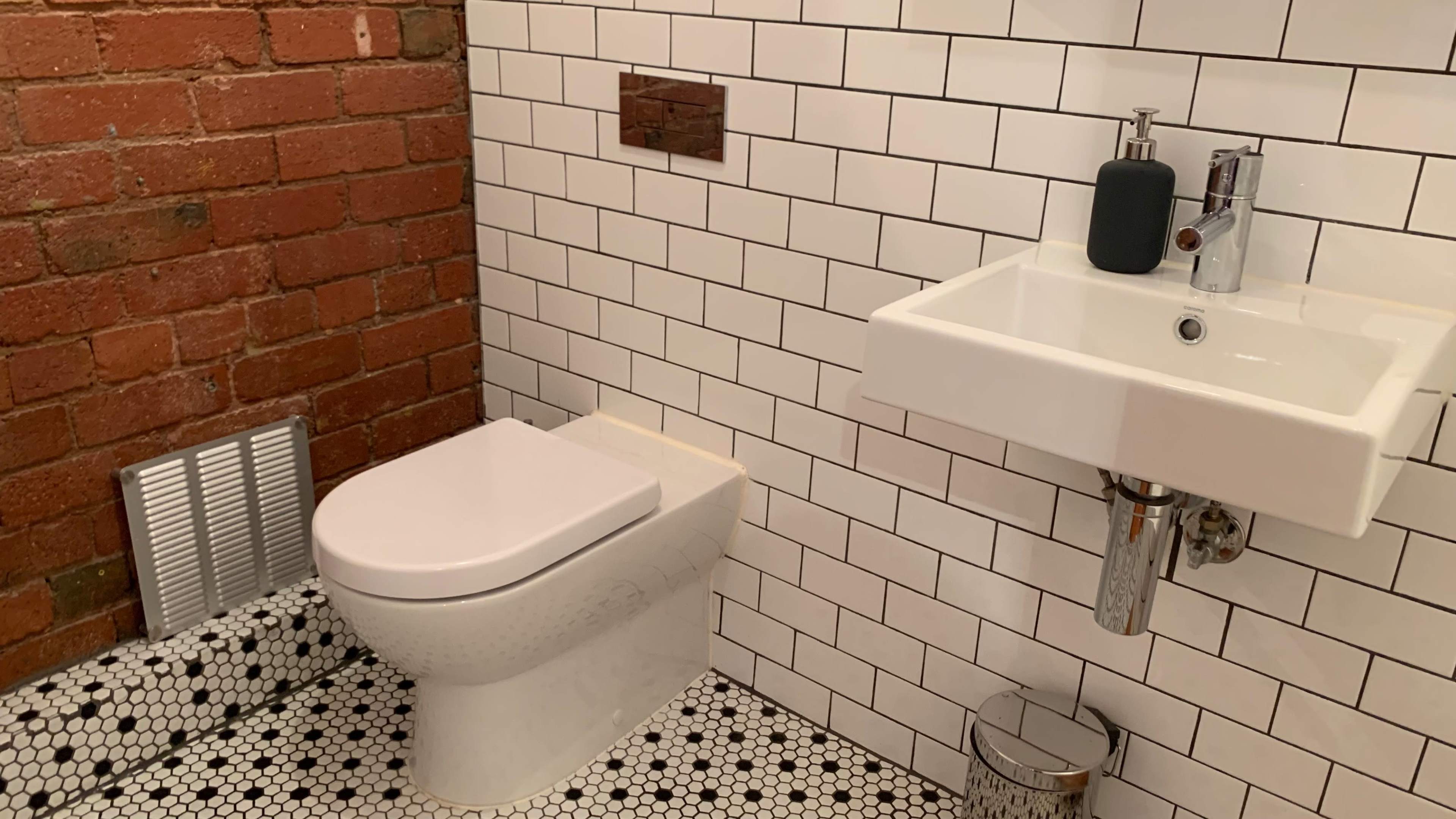 A bathroom featuring a modern toilet next to a wall-mounted sink, with white tiled walls and a patterned black-and-white floor.