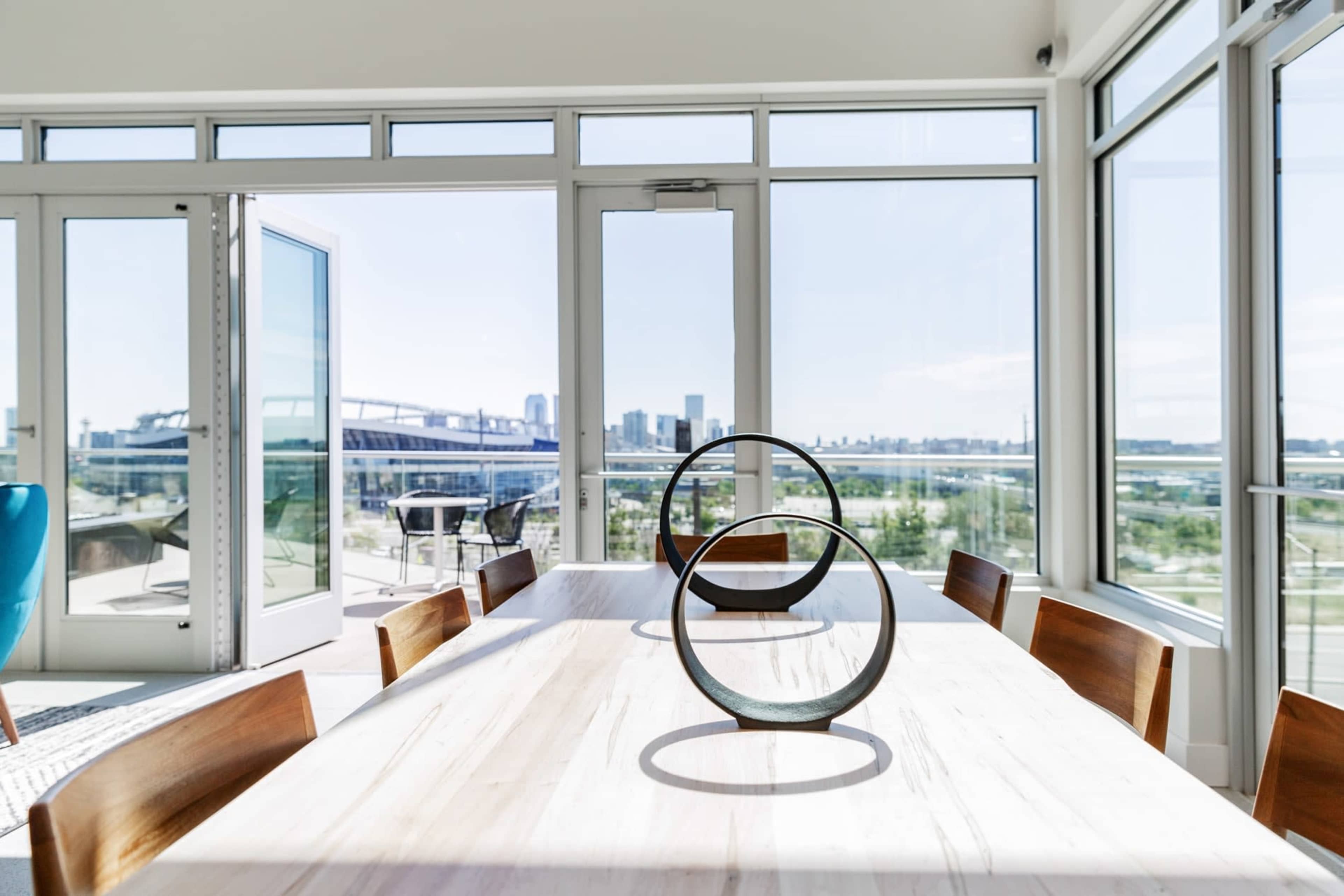 A modern dining area features a long wooden table with circular centerpieces and large windows offering a view of the city skyline.