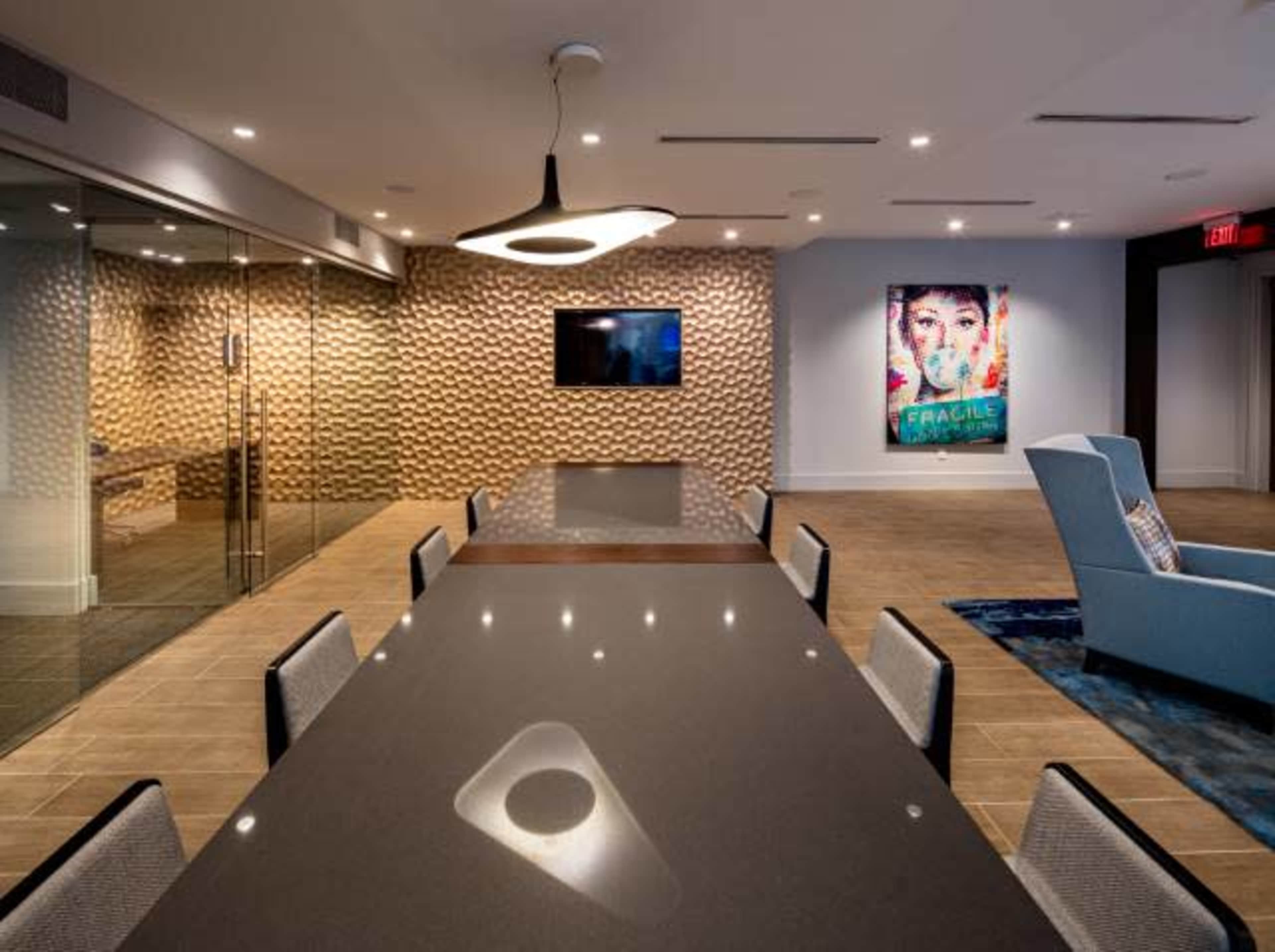 A modern conference room features a long dark table, a large TV, and decorative wall art, illuminated by stylish overhead lighting.
