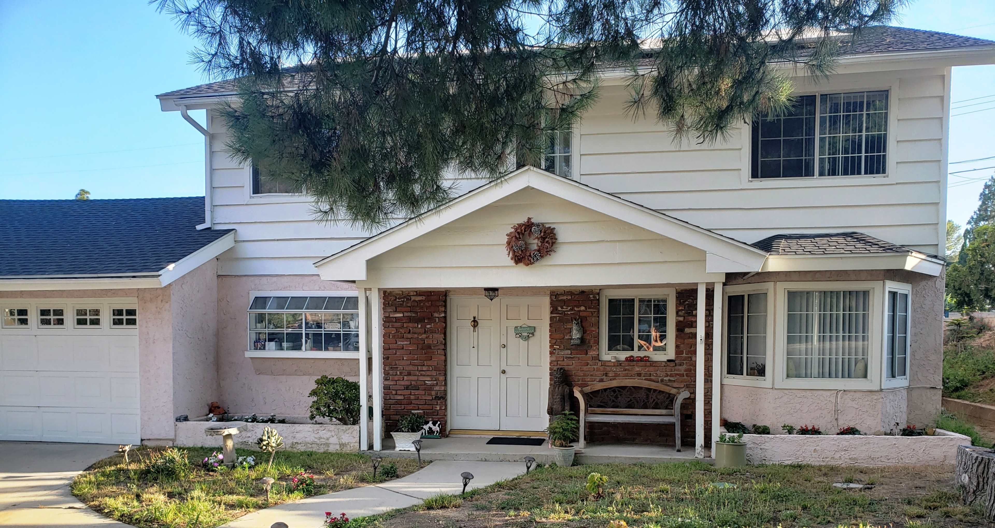 A two-story suburban house features a front porch, a brick accent wall, and a neatly landscaped yard.