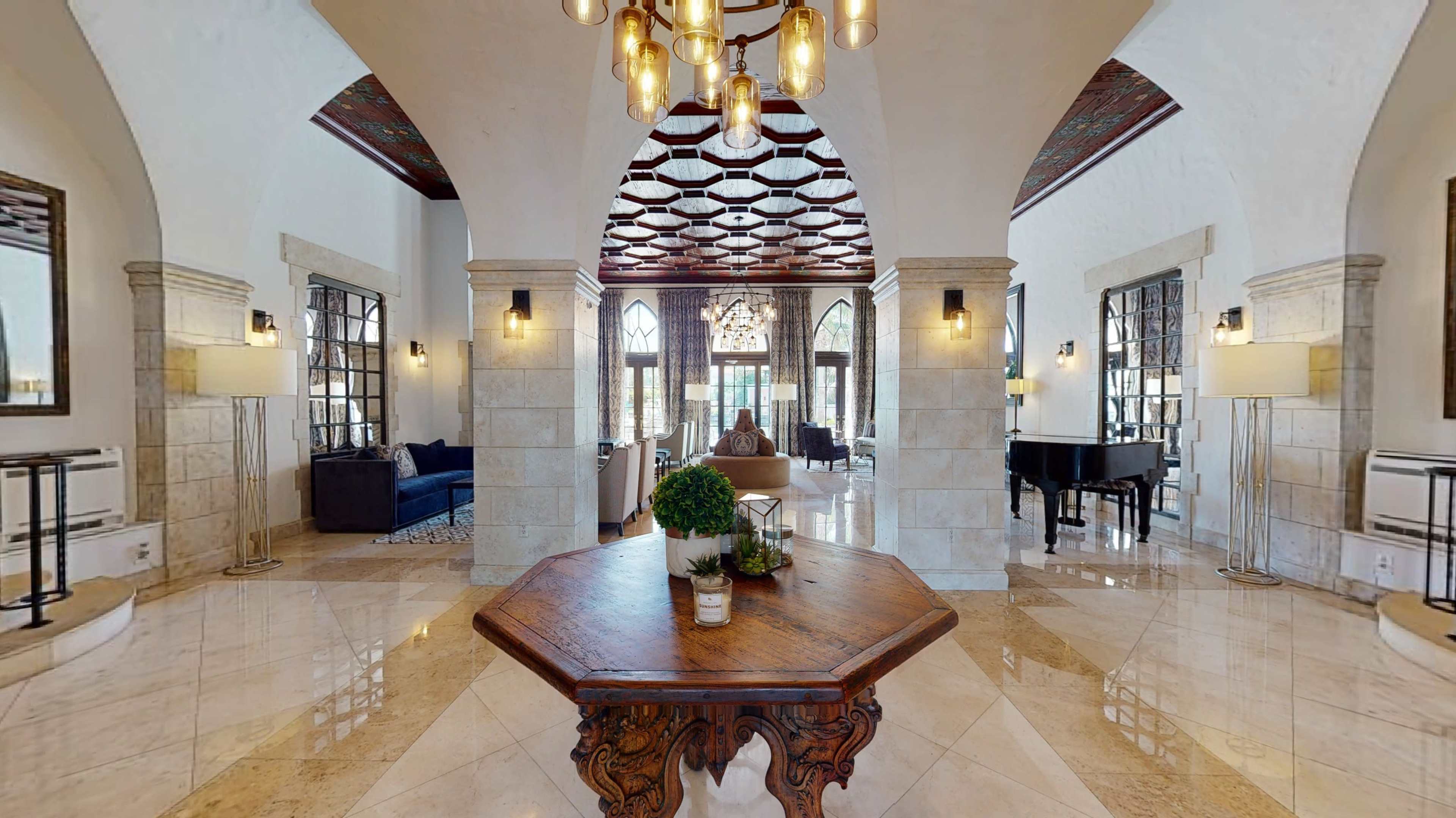 A spacious, elegantly designed lobby with a central wooden table, archways, and large windows letting in natural light.