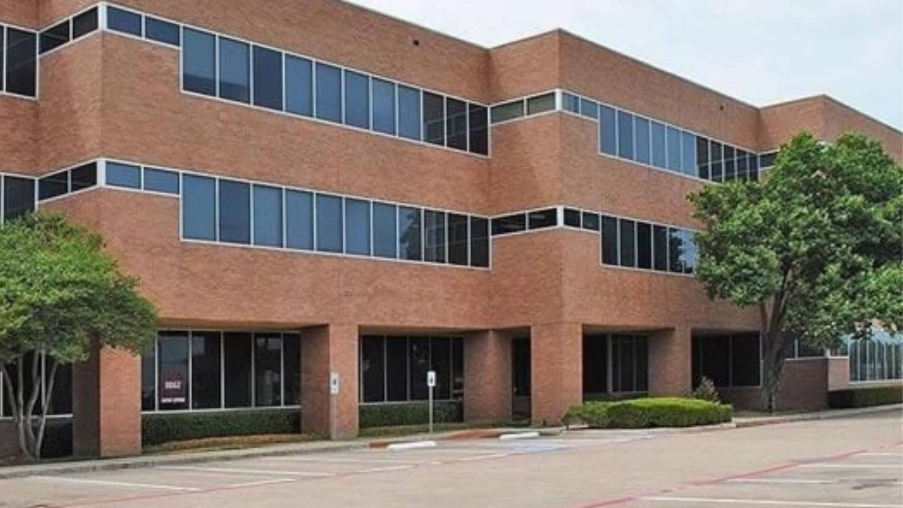 A multi-story brick office building with large windows and adjacent landscaping.