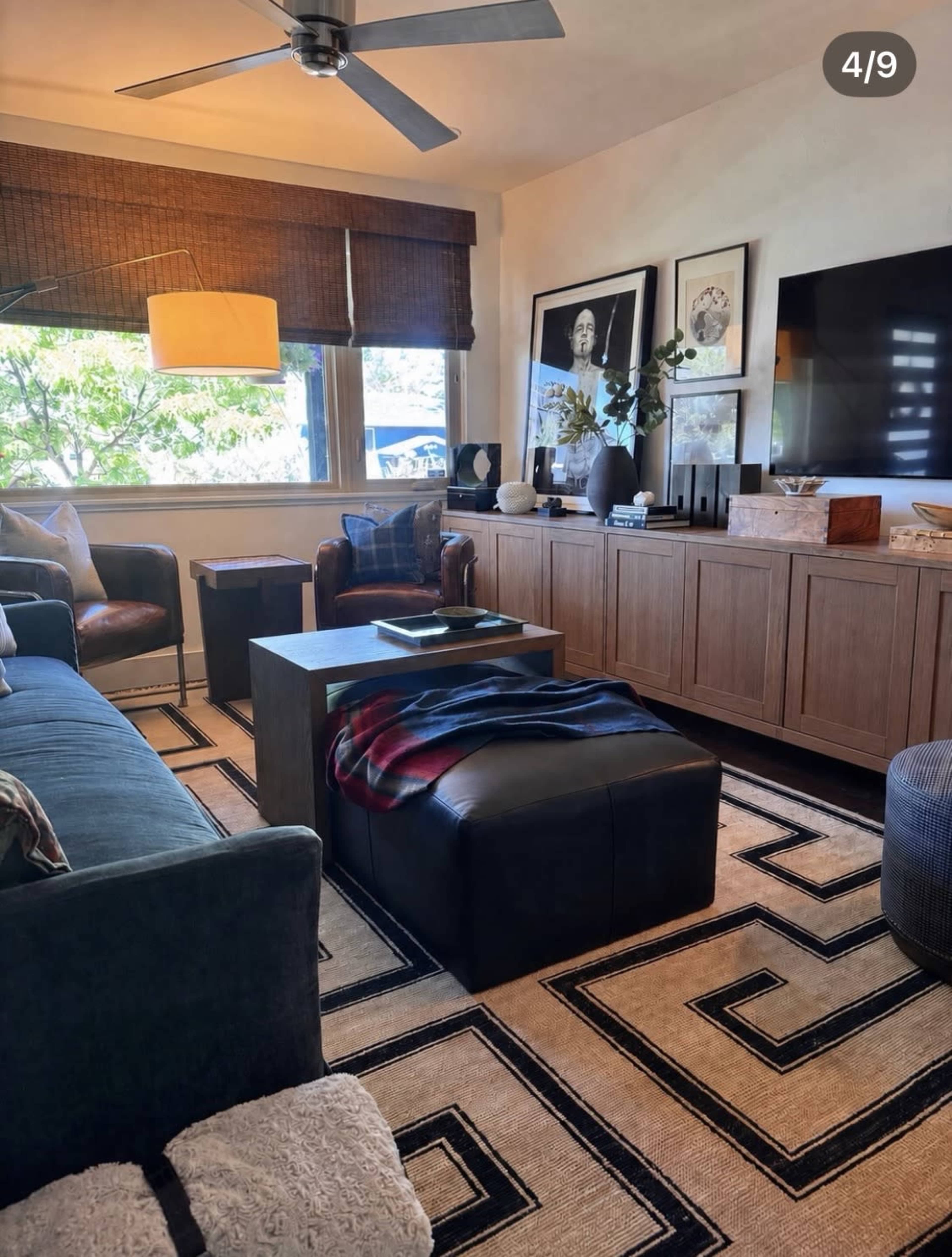 The image shows a cozy living room with a blue sofa, a coffee table in the center, a patterned rug, and a large TV mounted on the wall.