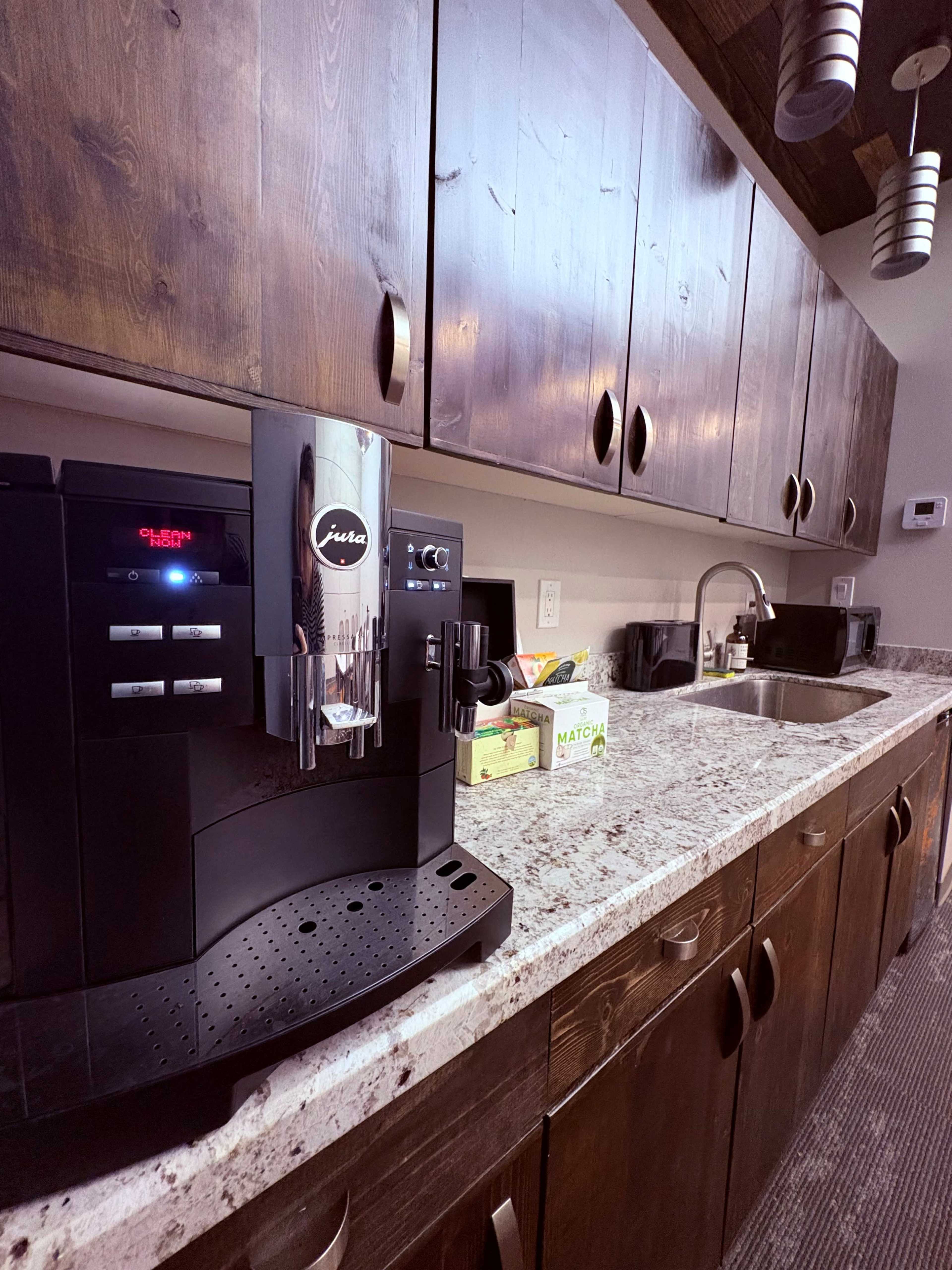 The image shows a modern kitchen countertop with a Jura coffee machine and a sink, alongside several kitchen cabinets and various items on the counter.