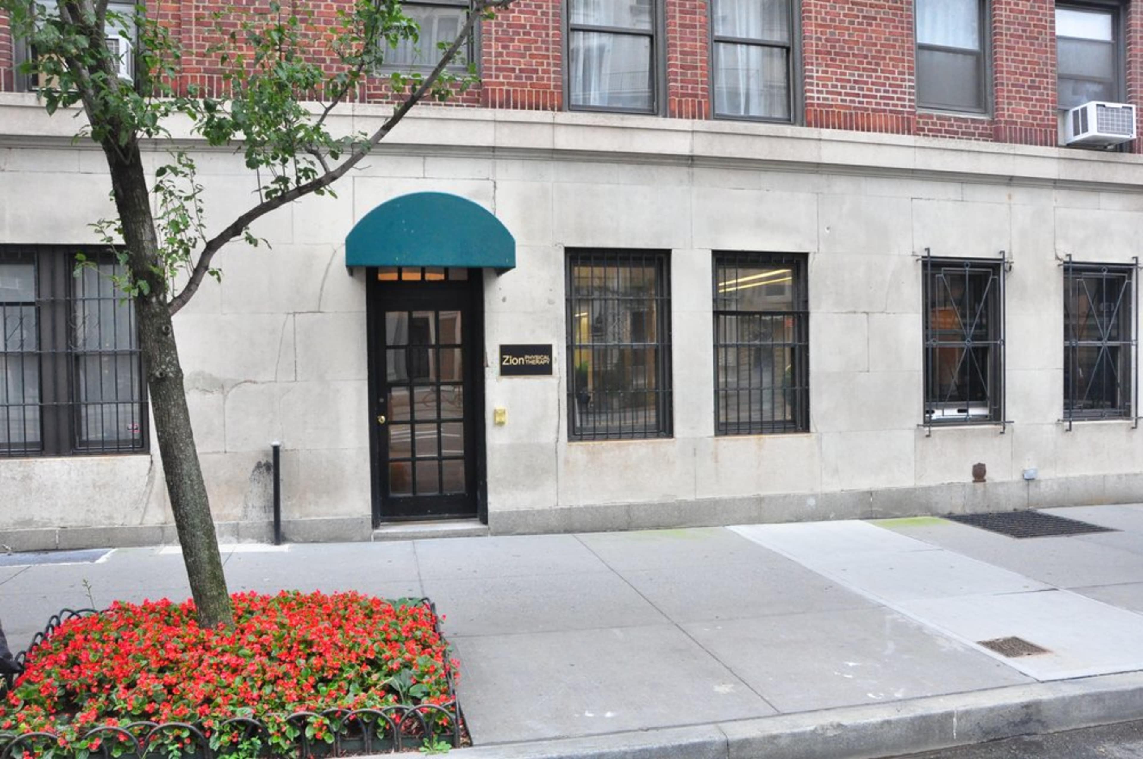 A building exterior with a sign labeled "Zionism," a small tree, and flower beds in front.