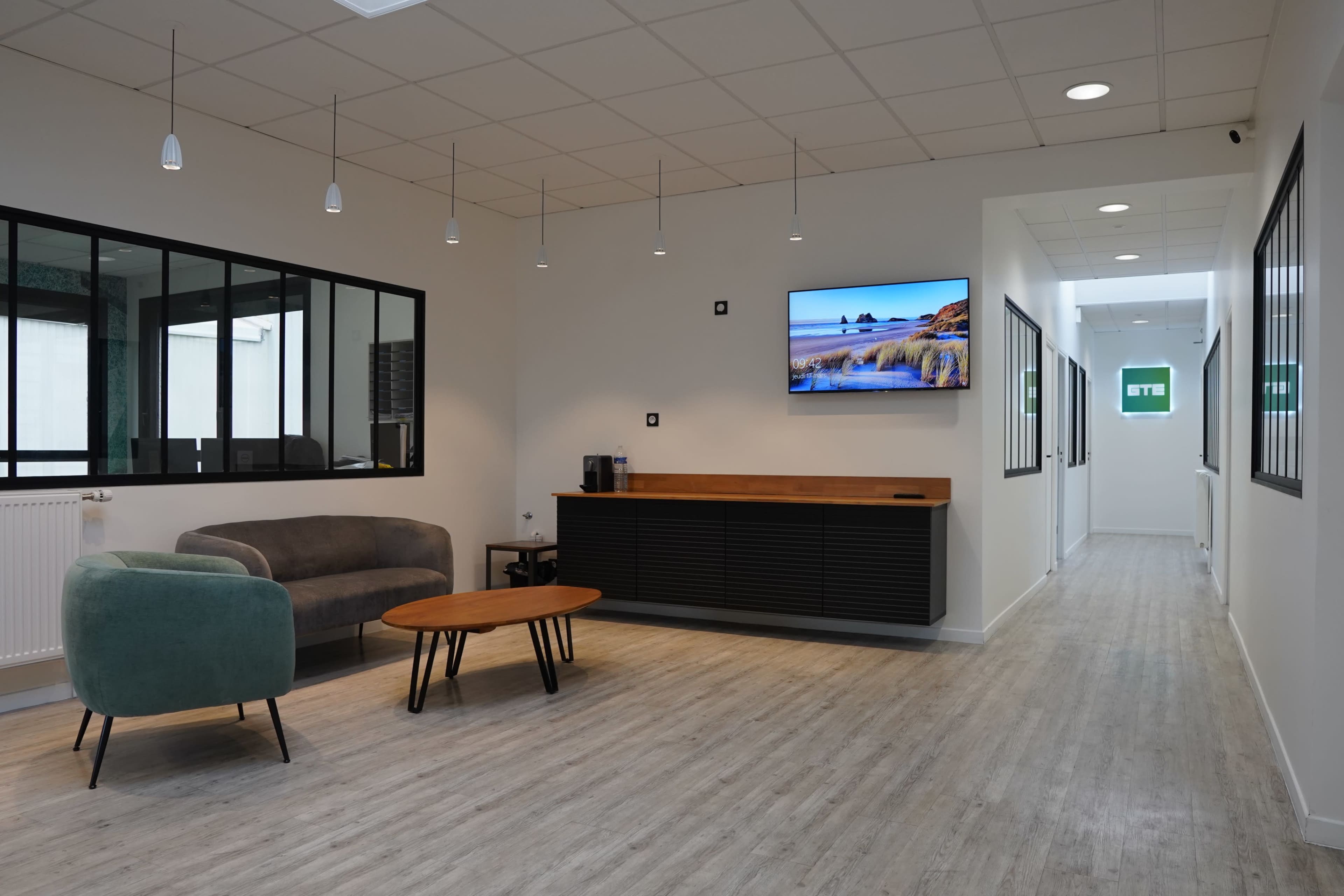 A contemporary office reception area featuring a green sofa, a wooden coffee table, and a wall-mounted television.