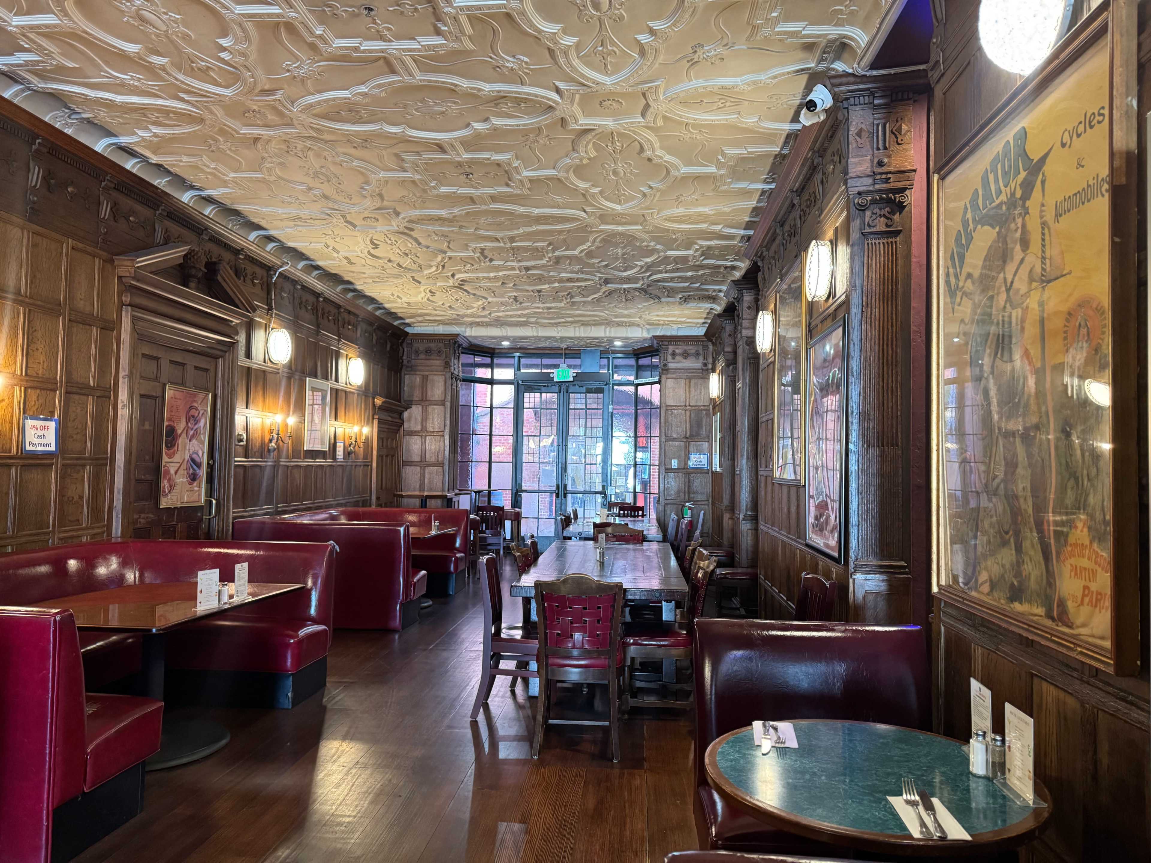 The image shows a restaurant interior with wood paneling, red upholstered booths, a large communal table, and ornate ceiling details.