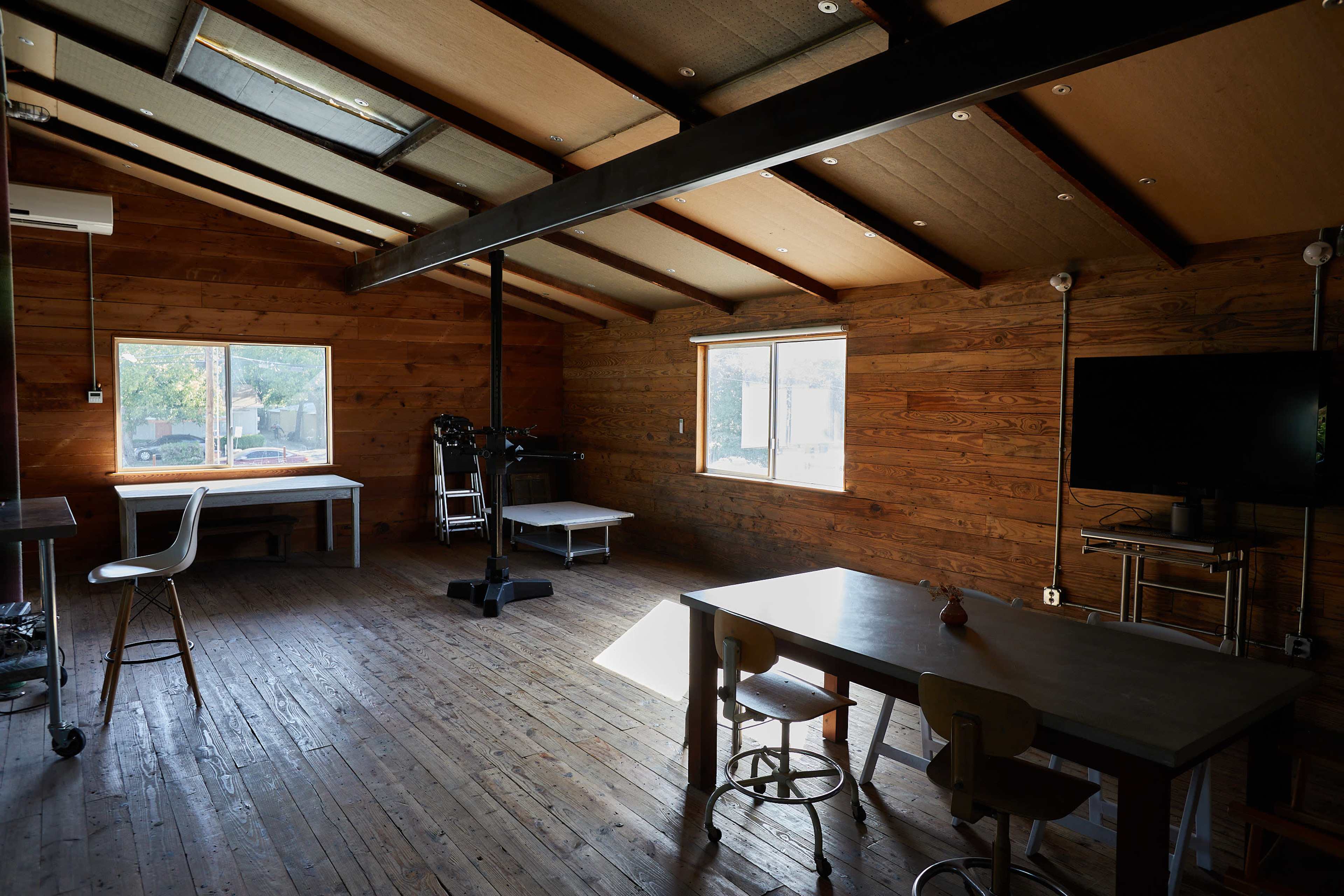 A wooden room with a high ceiling, featuring large windows, a table with chairs, and a television set.