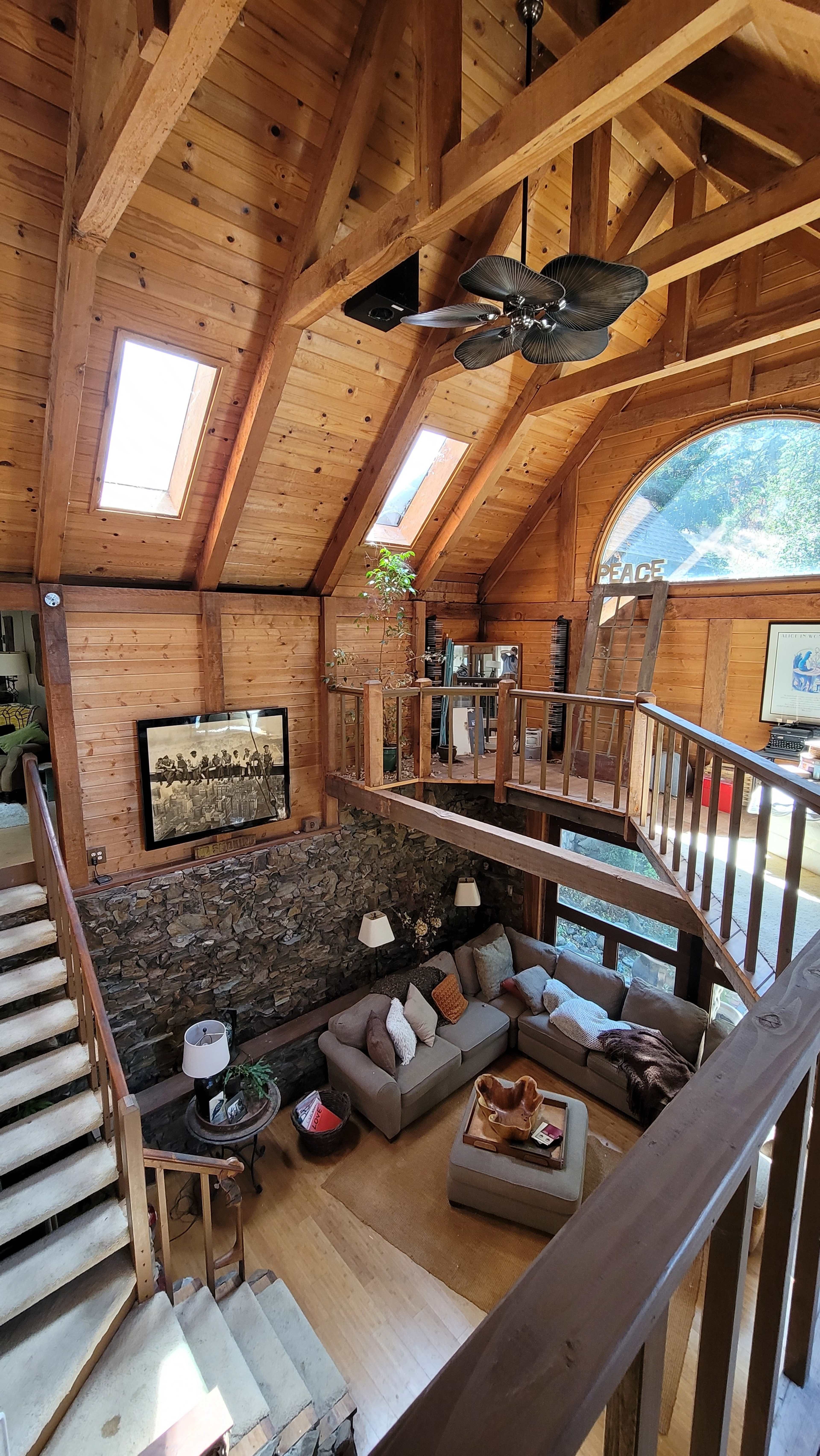 A spacious wooden living room with a stone accent wall, large windows, and a staircase leading to an upper level.