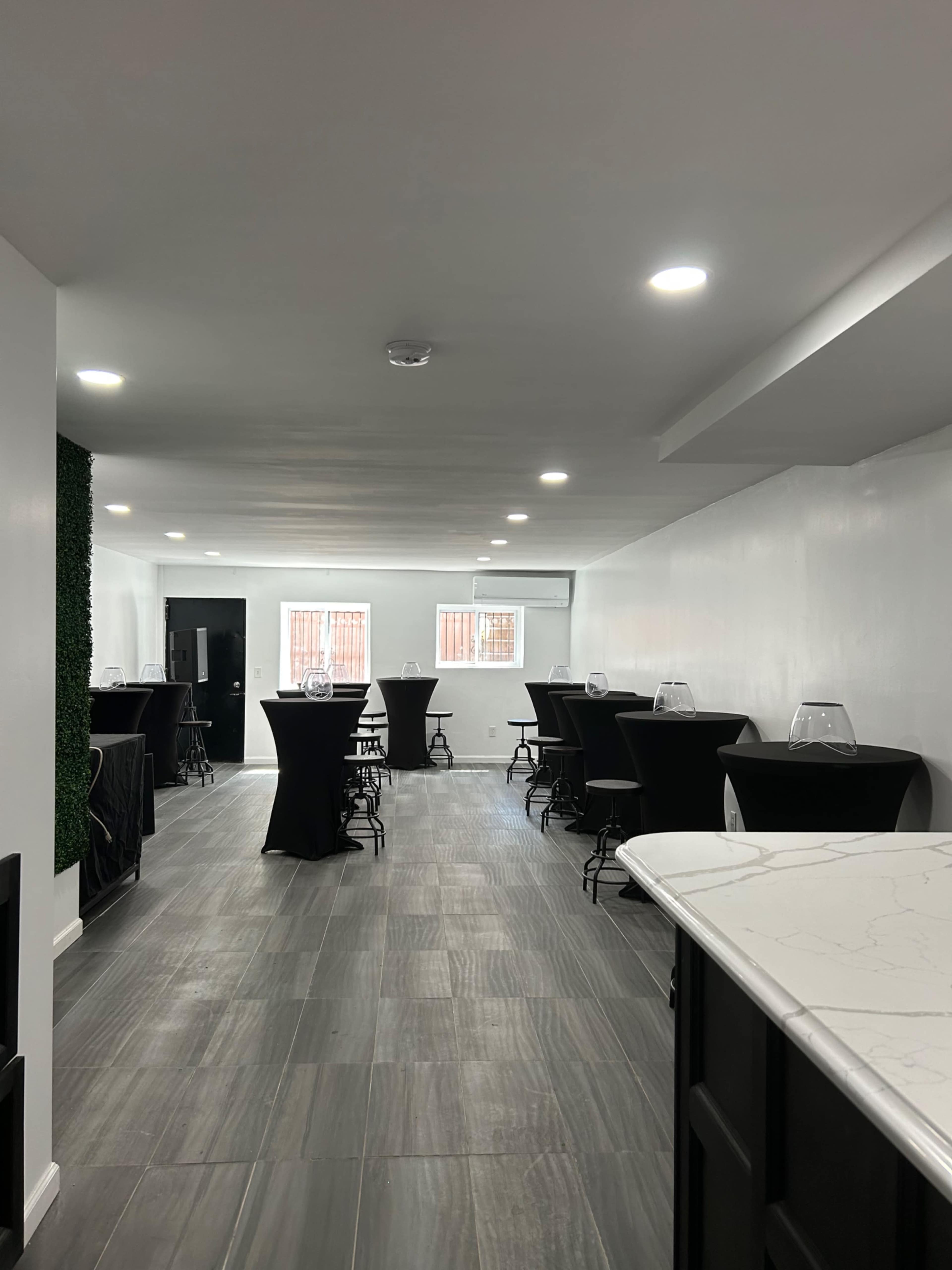 The image shows a spacious event room with several high-top tables covered in black cloth and illuminated by ceiling lights.