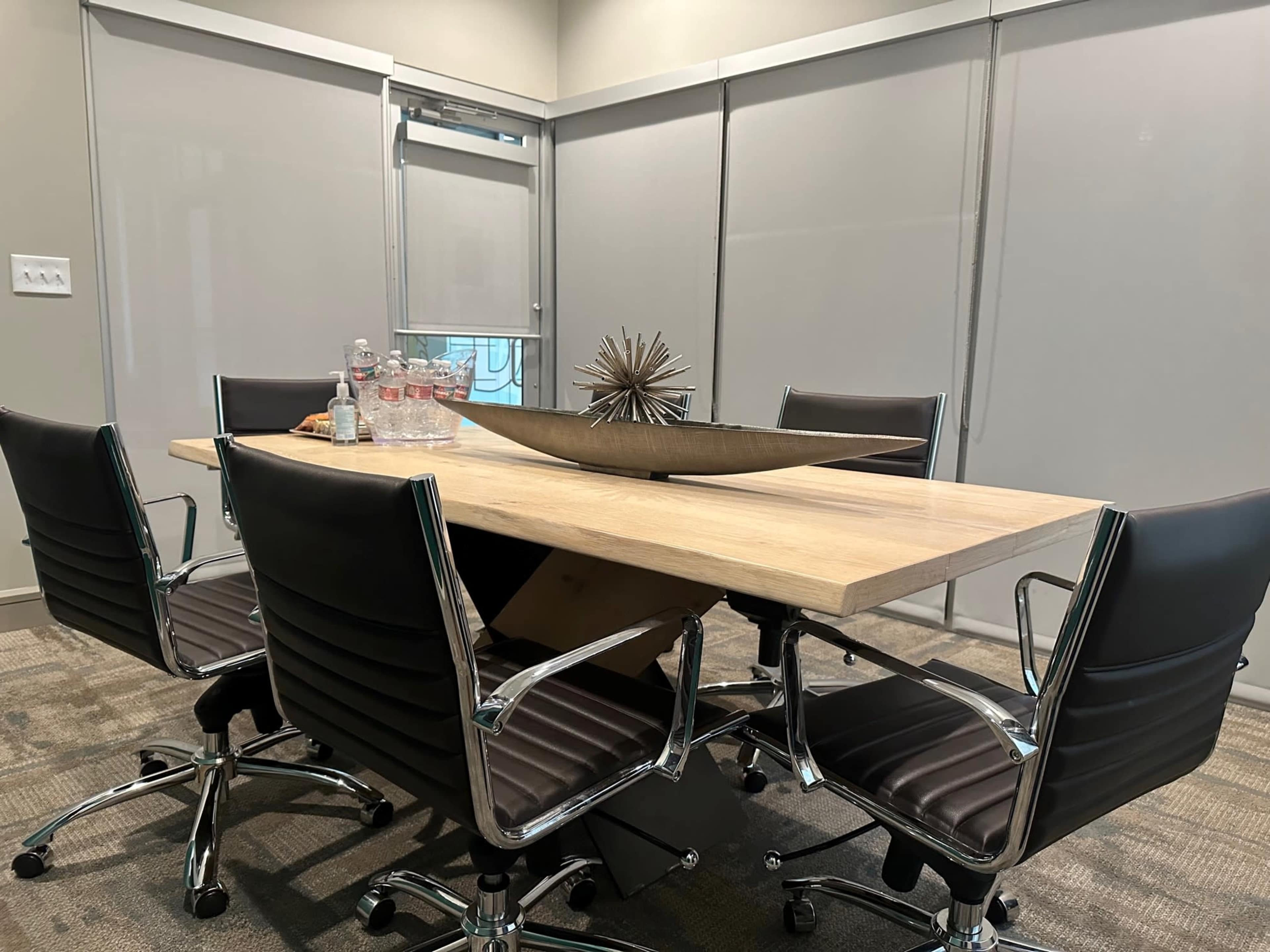 A modern conference room features a wooden table surrounded by five black chairs and a decorative centerpiece.