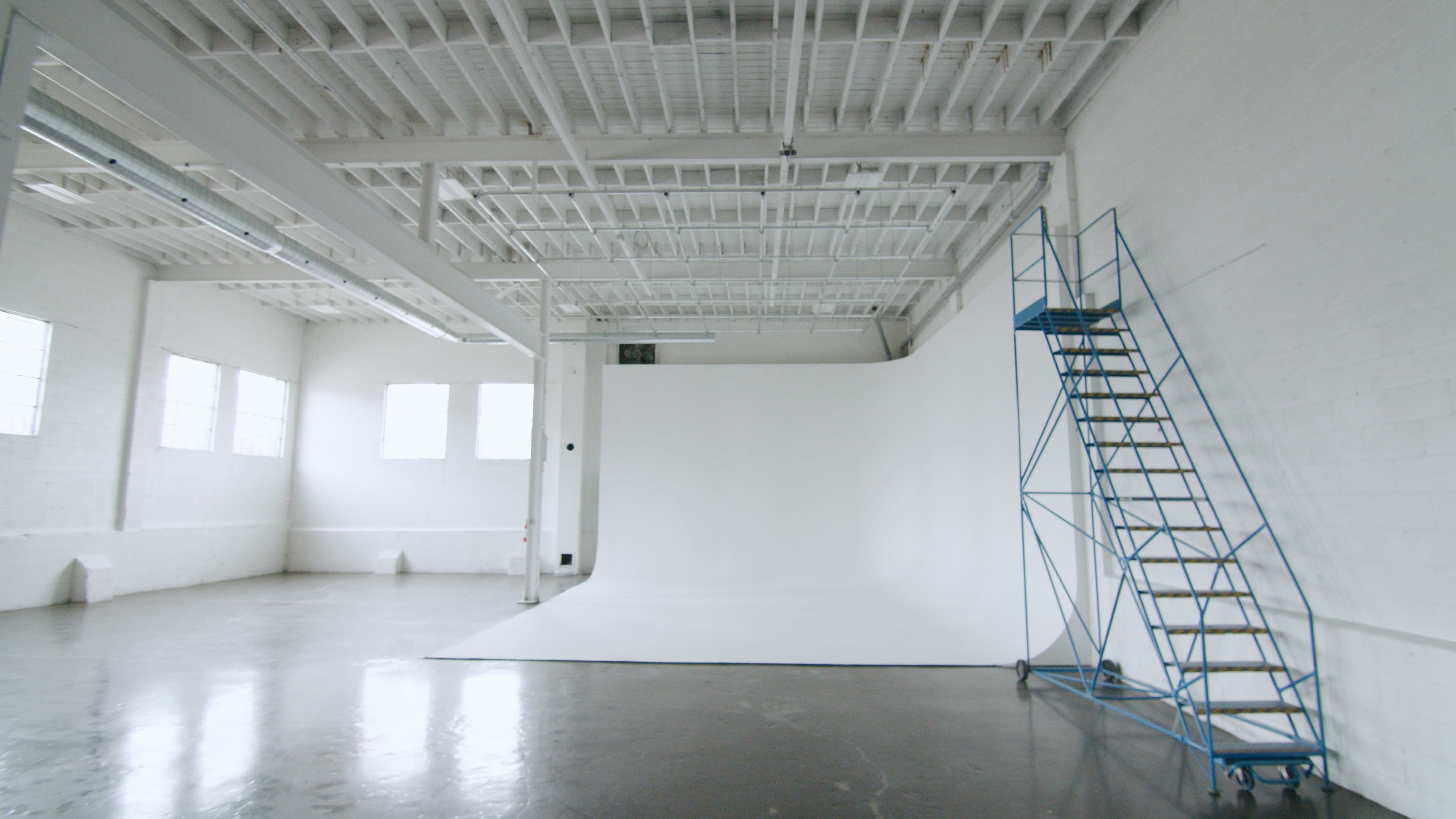 A spacious photography studio with a white seamless backdrop and a blue metal scaffolding on the side.