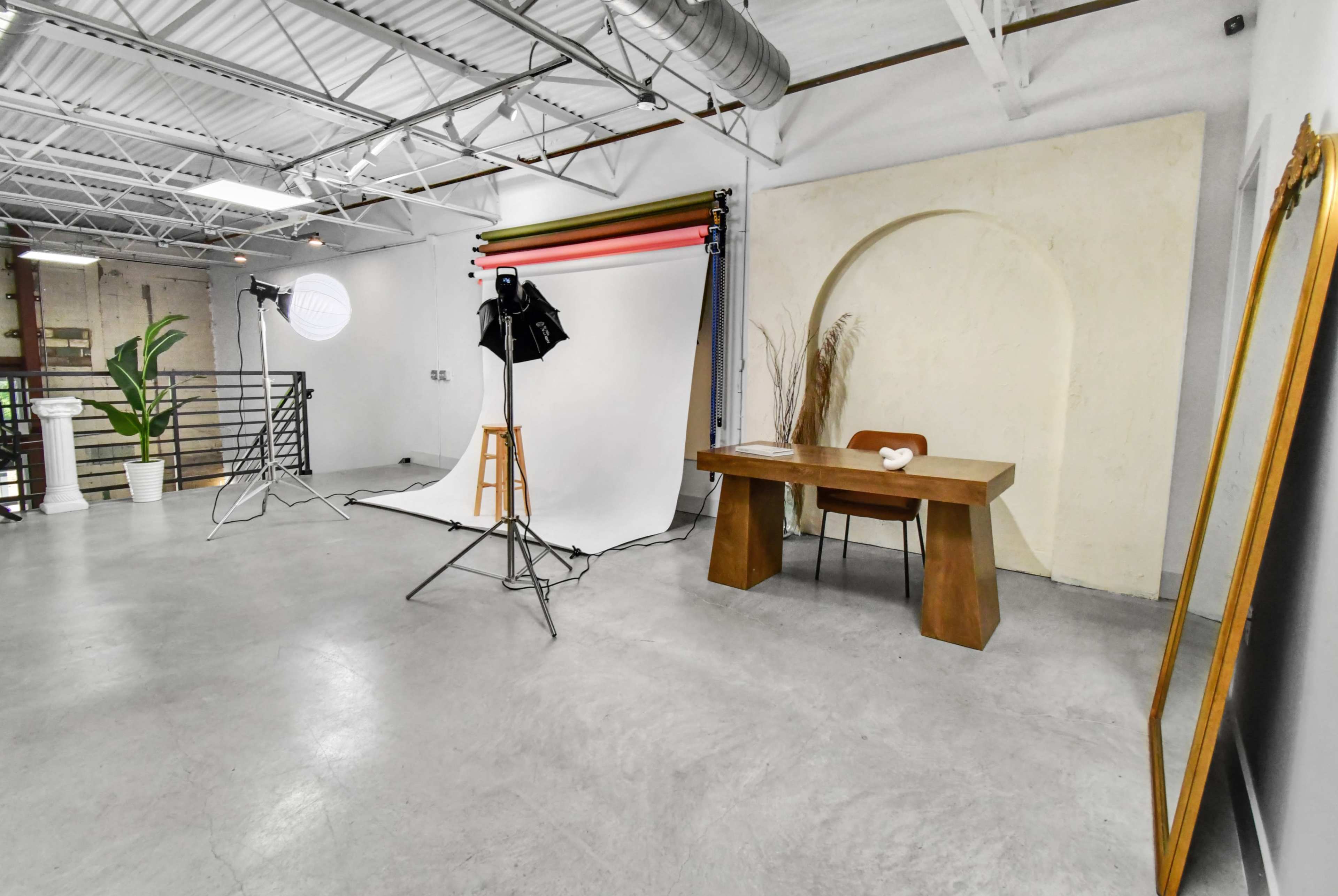 The image shows a spacious studio with a photography setup, featuring a backdrop, lighting equipment, and a wooden table against a textured wall.