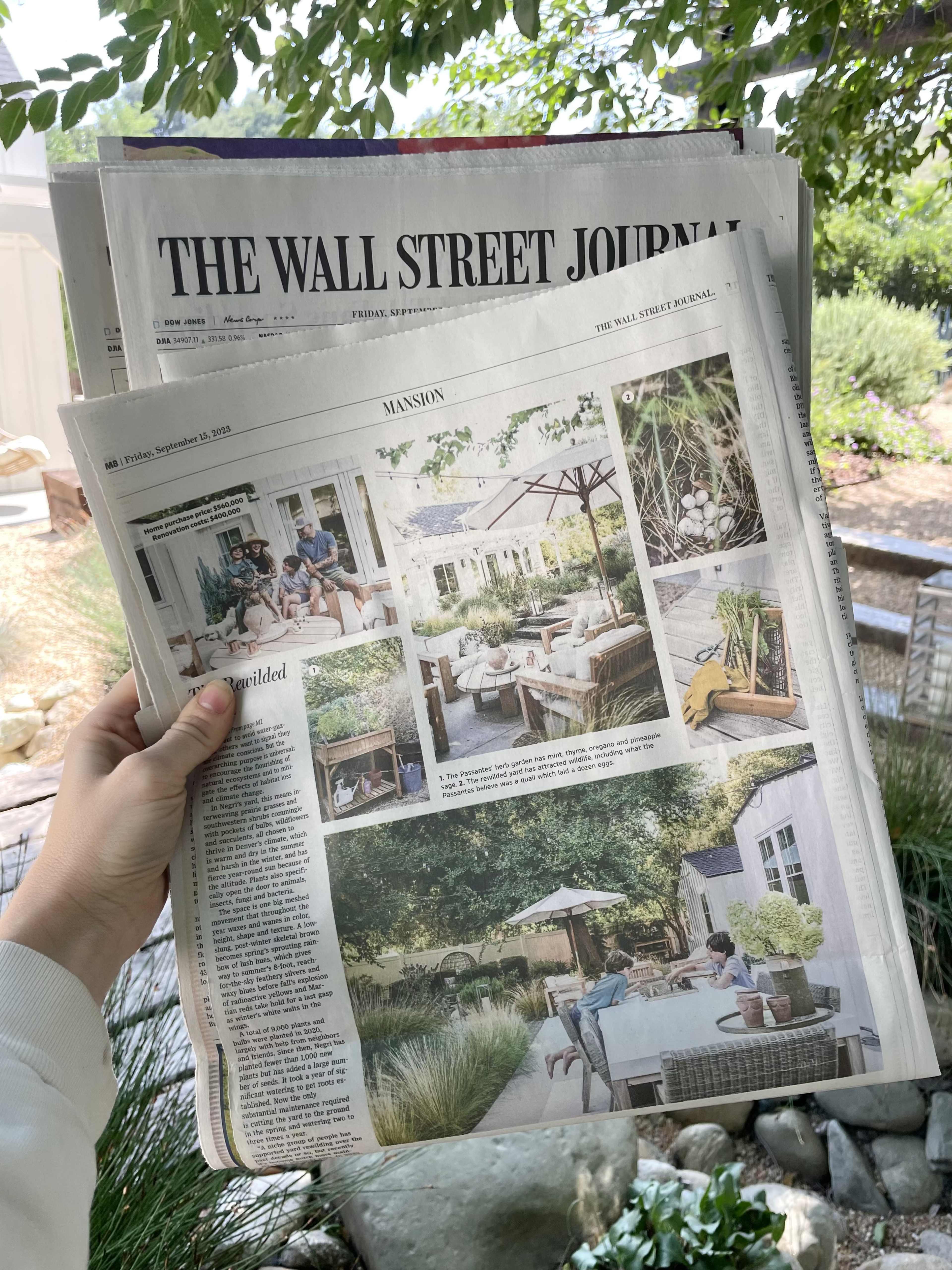 A person holds a copy of The Wall Street Journal featuring a lifestyle section with images of a garden and outdoor seating.