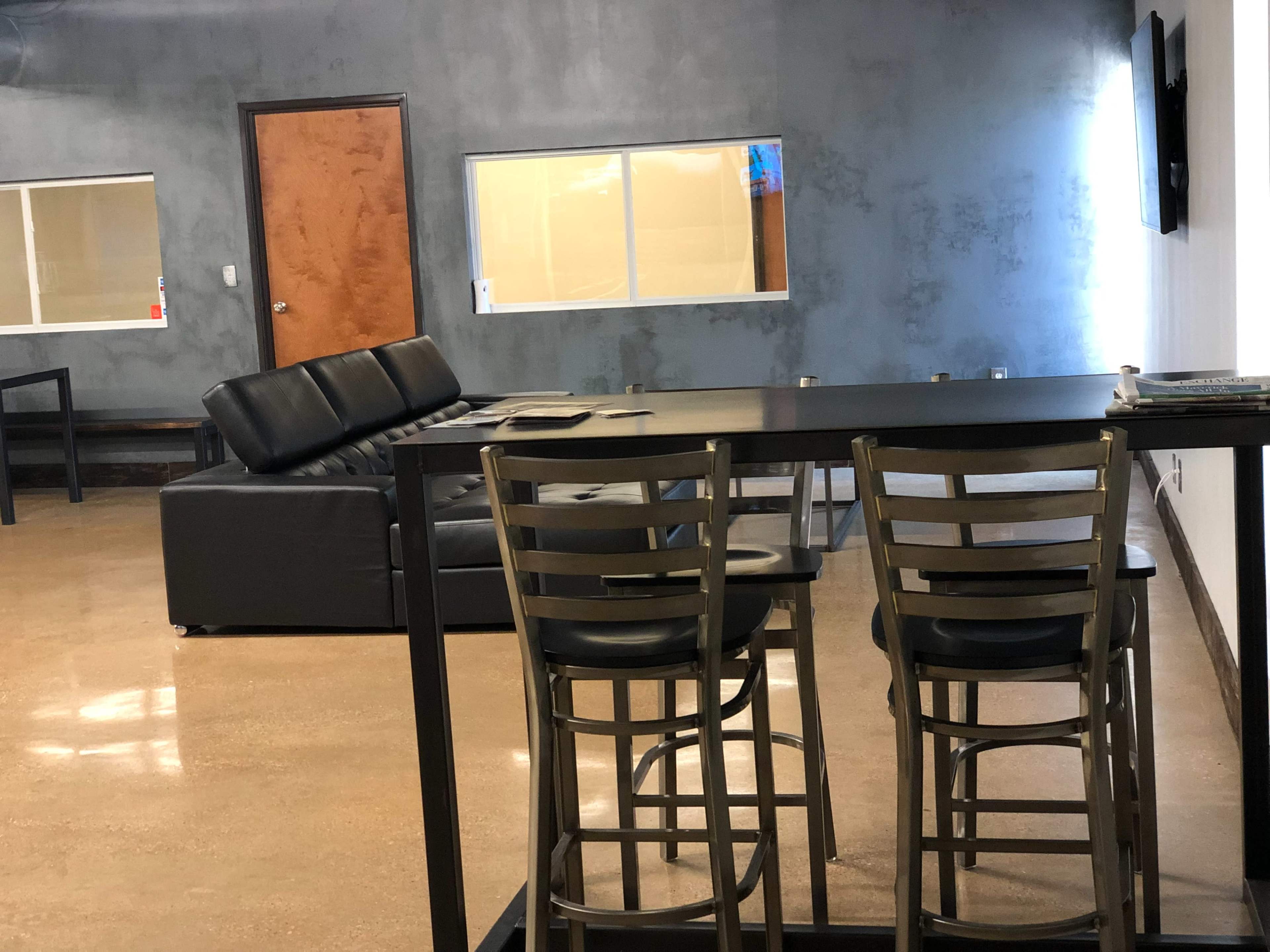 The image shows a modern interior with a black leather couch and a tall table with metal chairs, set against a gray wall.