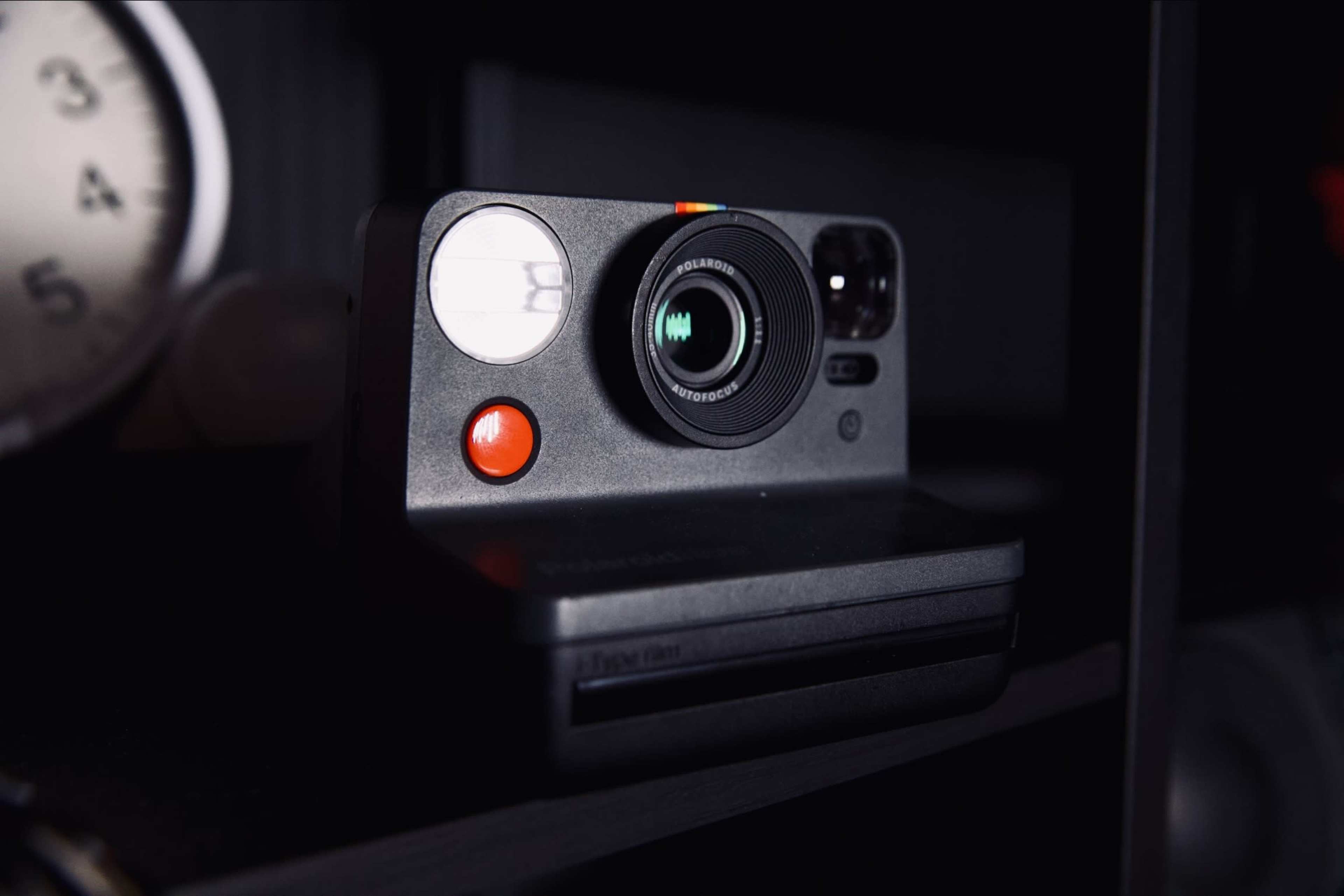 A black instant camera rests on a shelf next to a round clock.