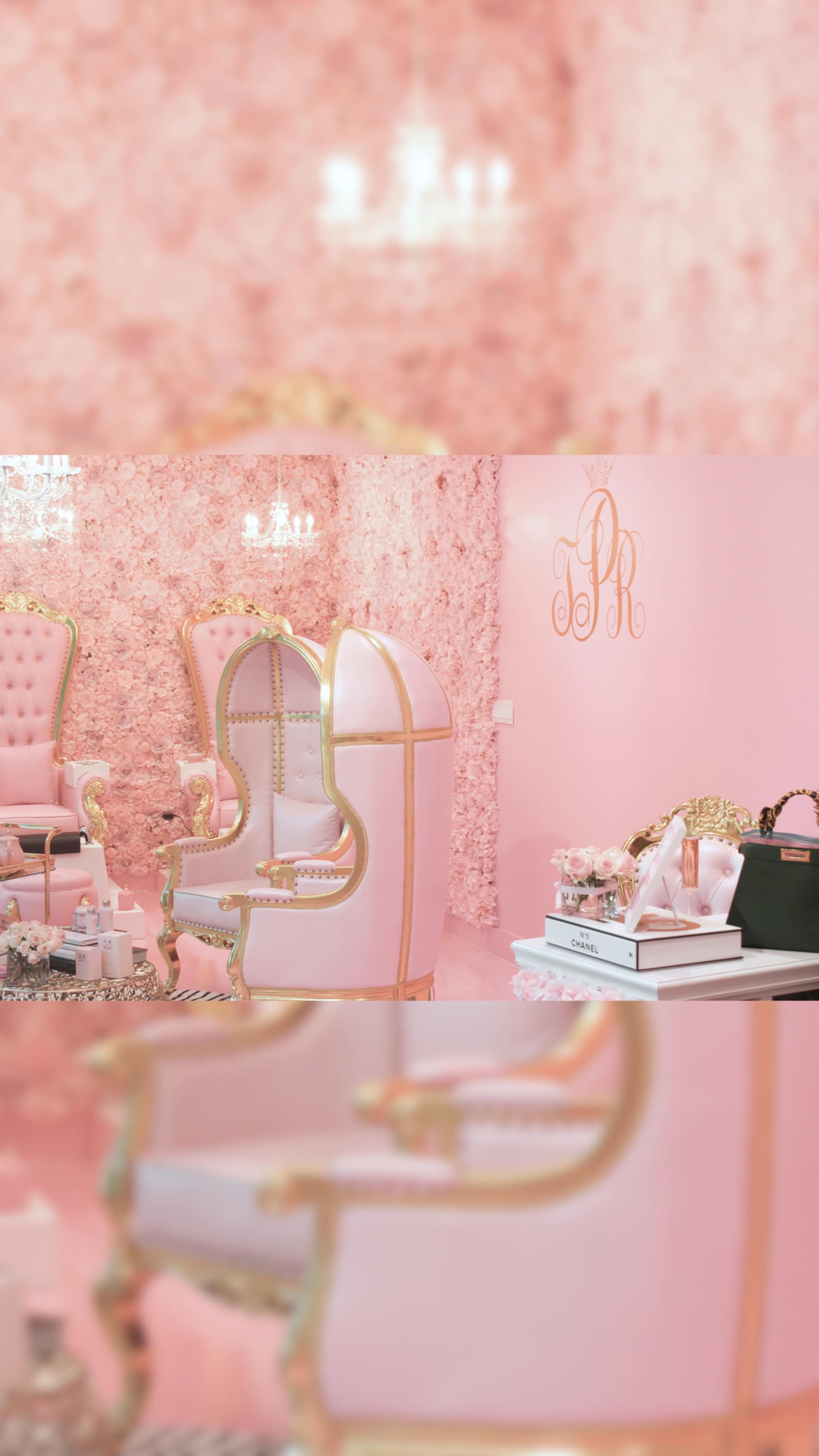 A luxurious beauty salon features pink velvet chairs with gold accents and a floral wall backdrop.