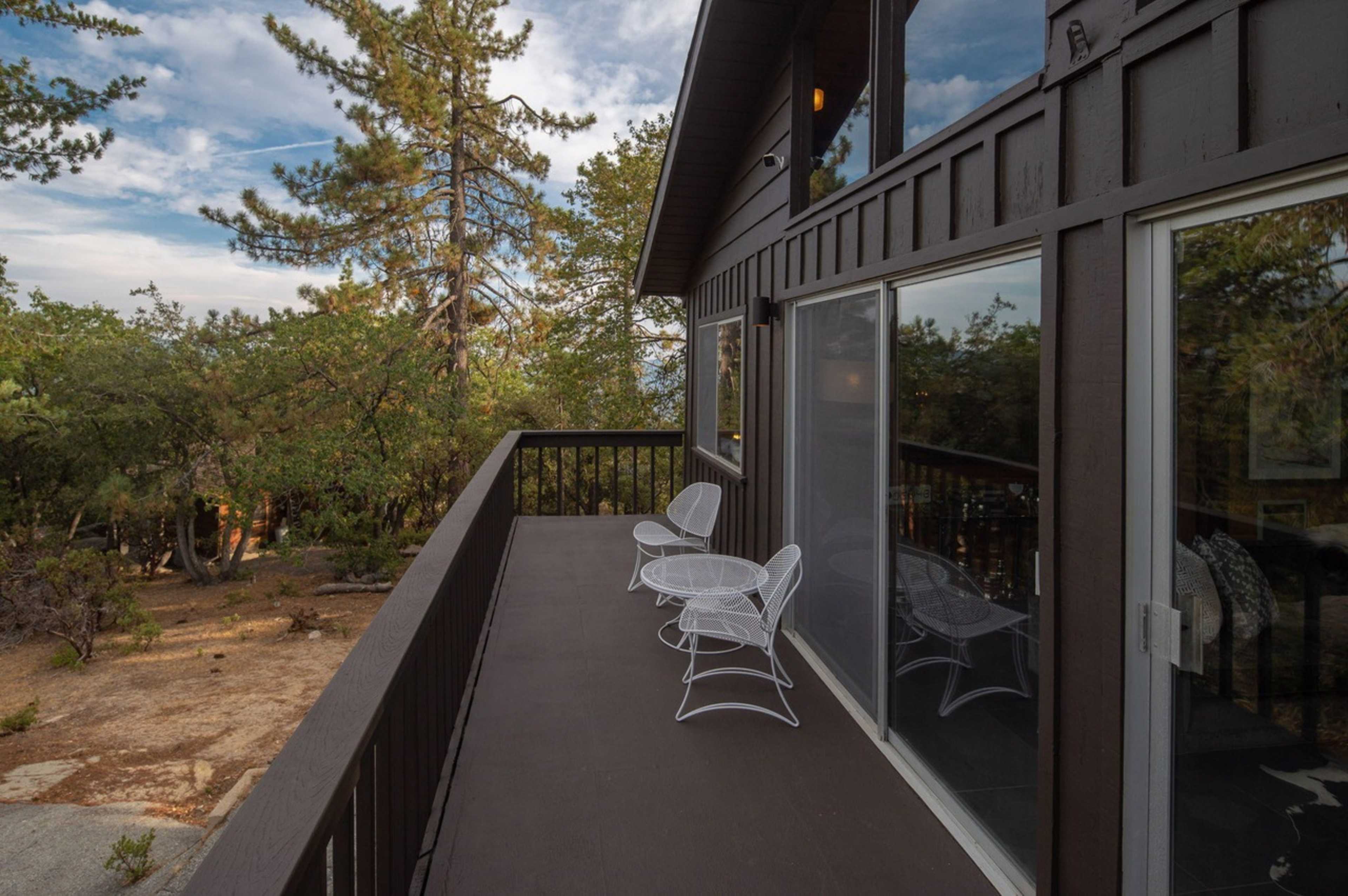 A wooden deck with two white chairs overlooks a wooded landscape.