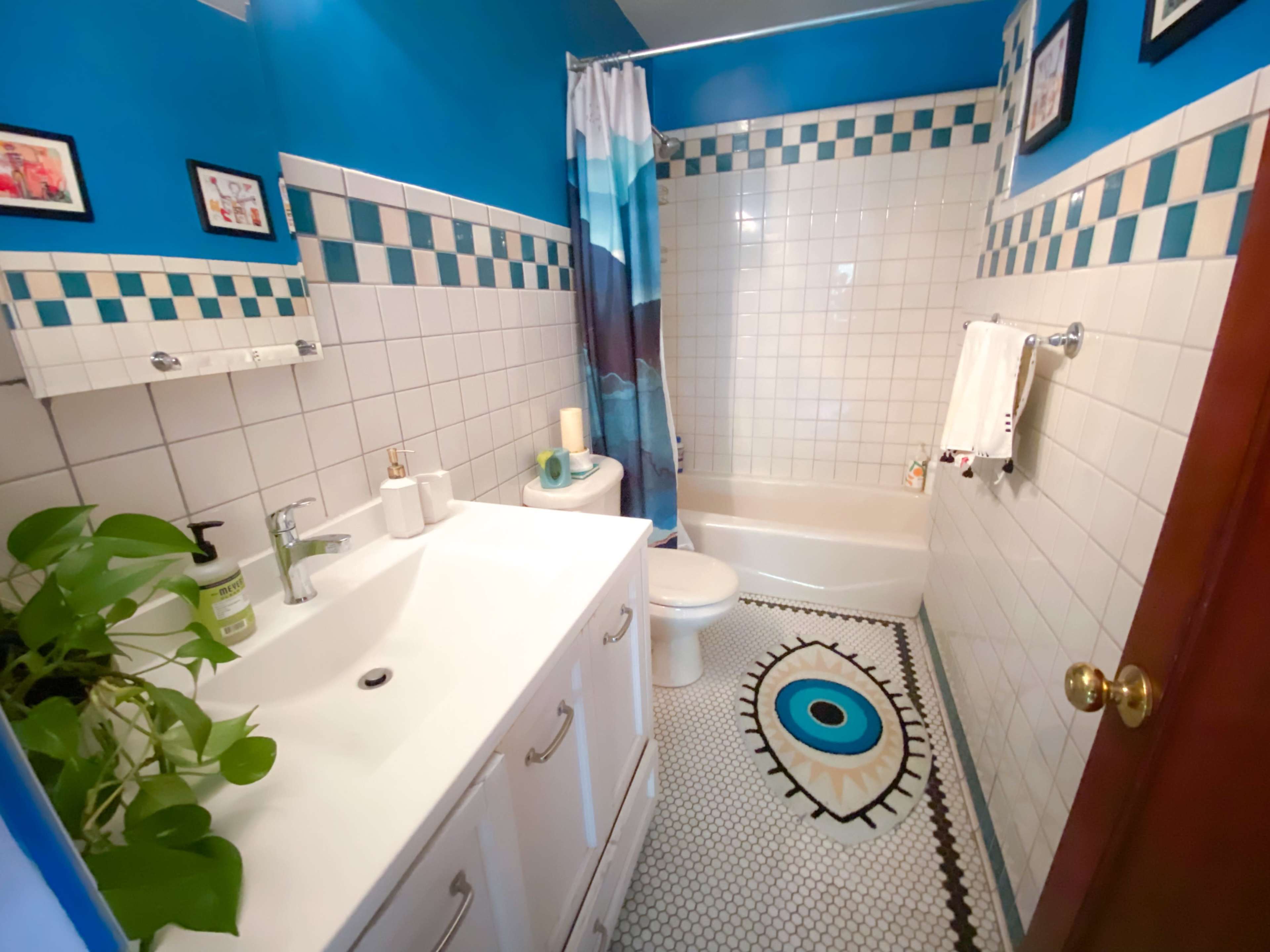 The image shows a small bathroom featuring a shower-tub combination, a white vanity with a sink, and decorative tile work on the walls and floor.