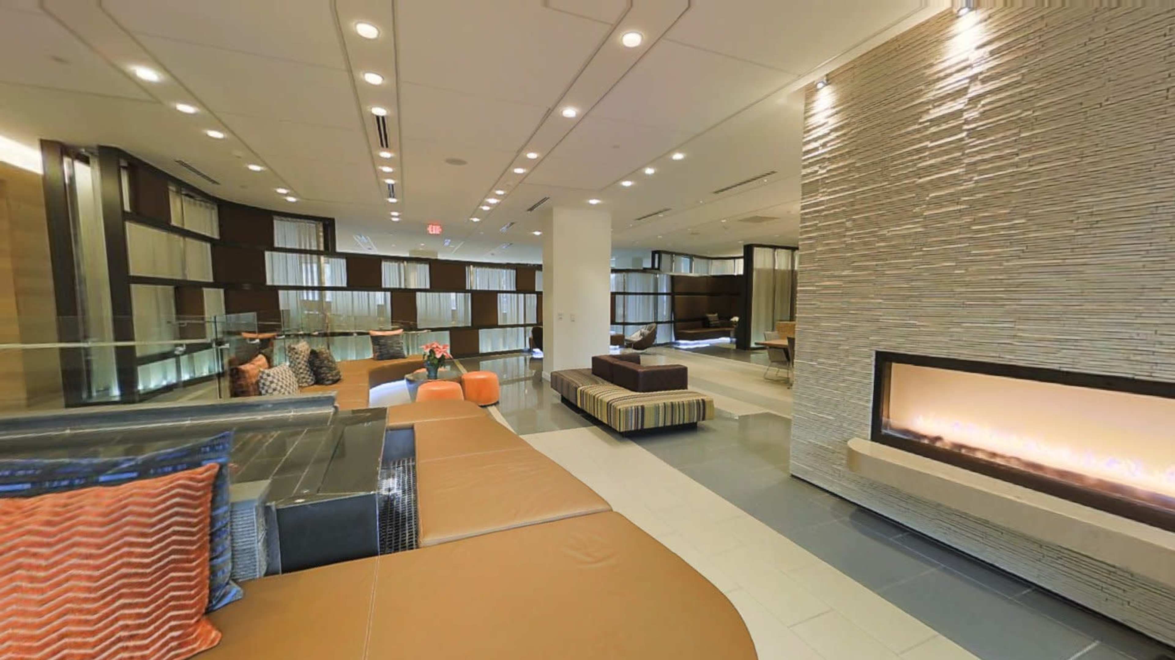 A modern lobby area featuring comfortable seating, a decorative stone wall, and a linear fireplace.