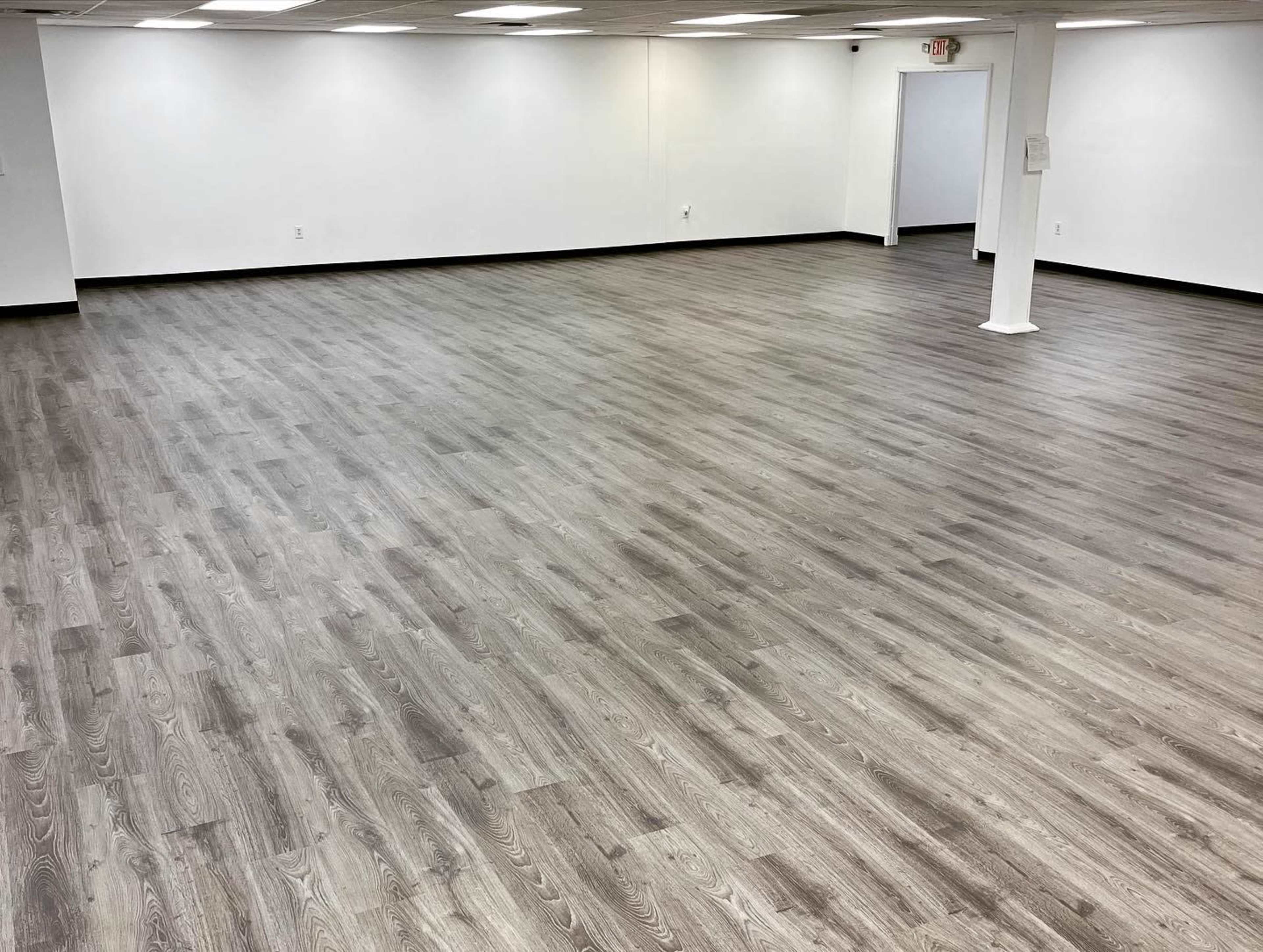 A spacious, empty room with light gray wood flooring and white walls.