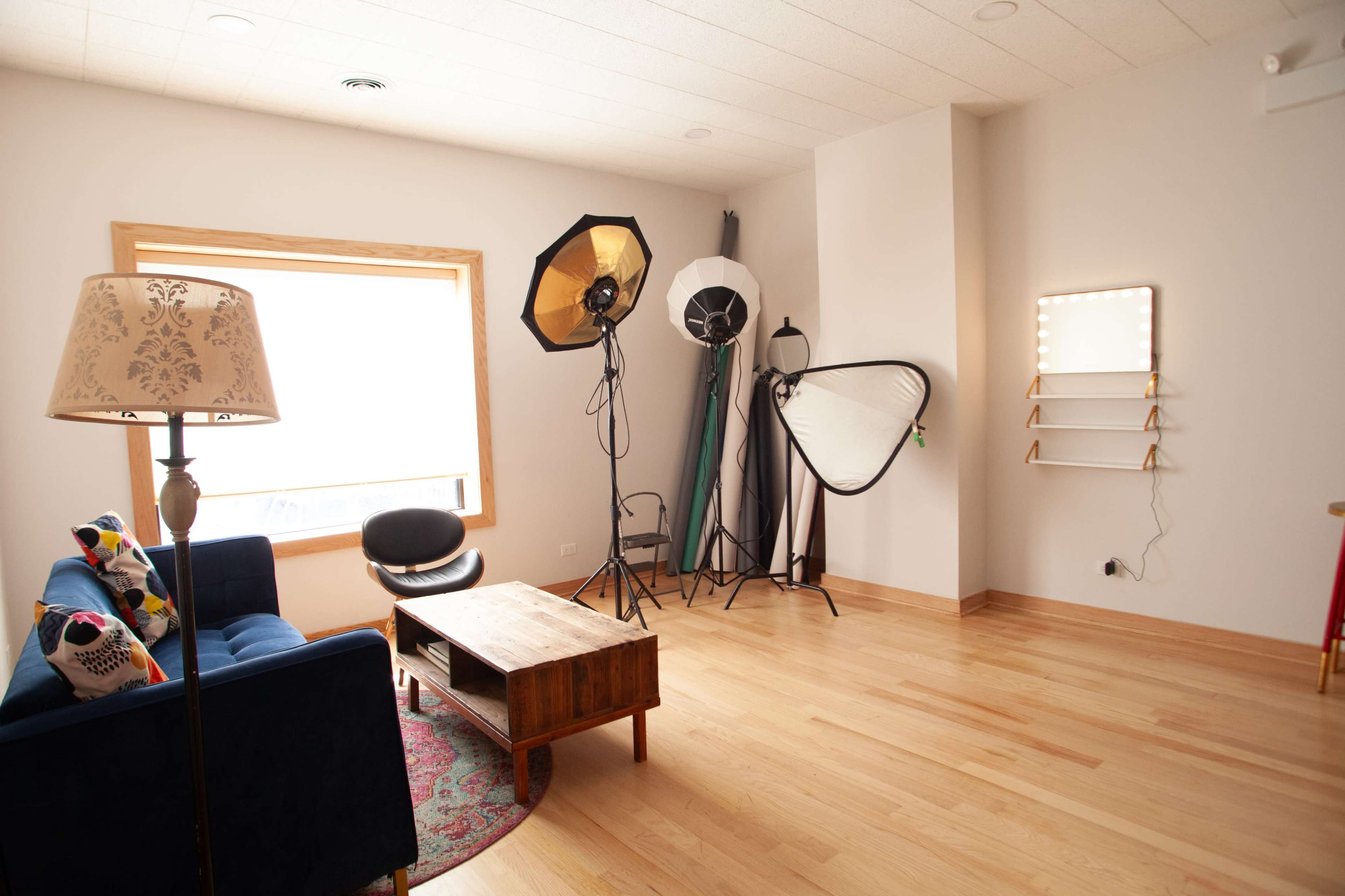 A well-lit photography studio features a blue couch, a wooden coffee table, and various lighting equipment in a spacious room.