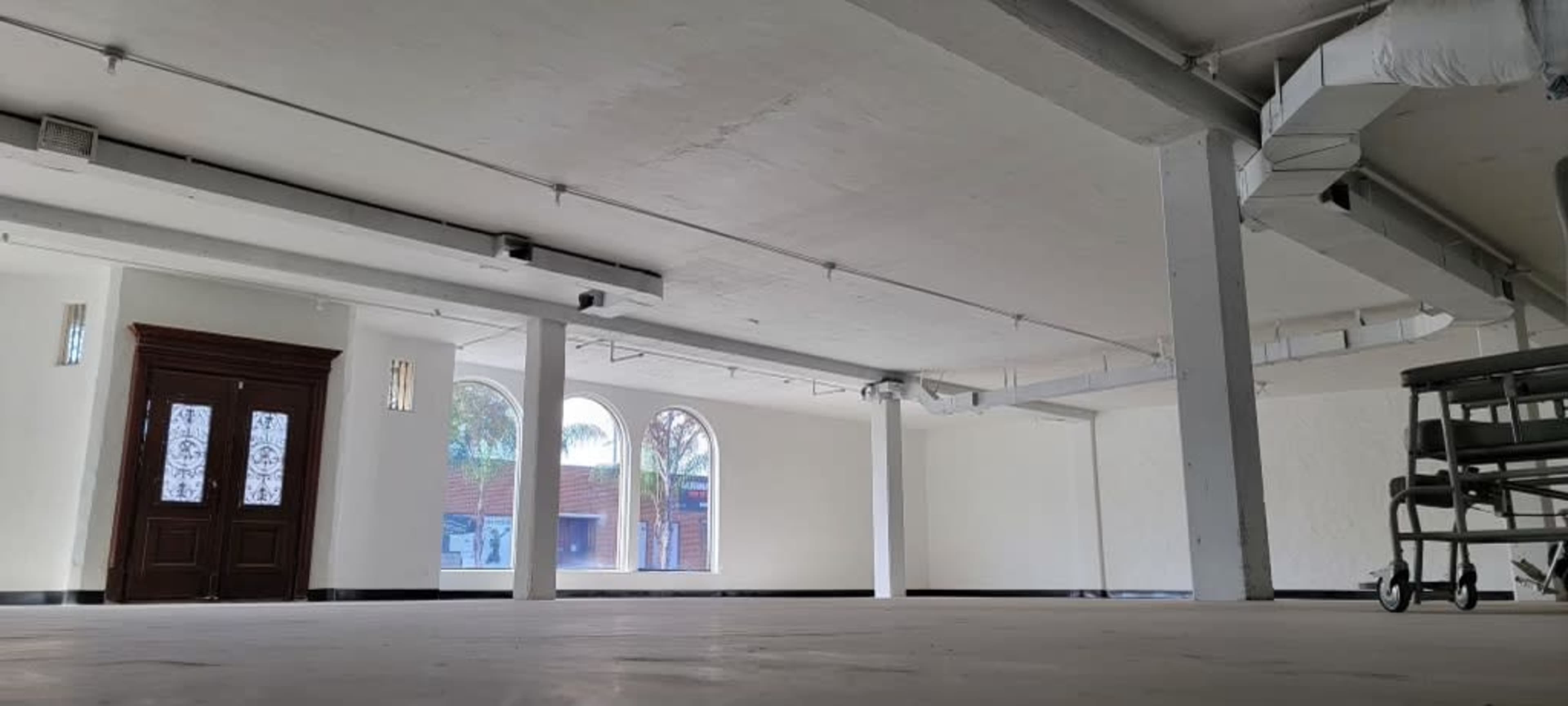 A spacious, empty interior room with large arched windows and a set of double doors.