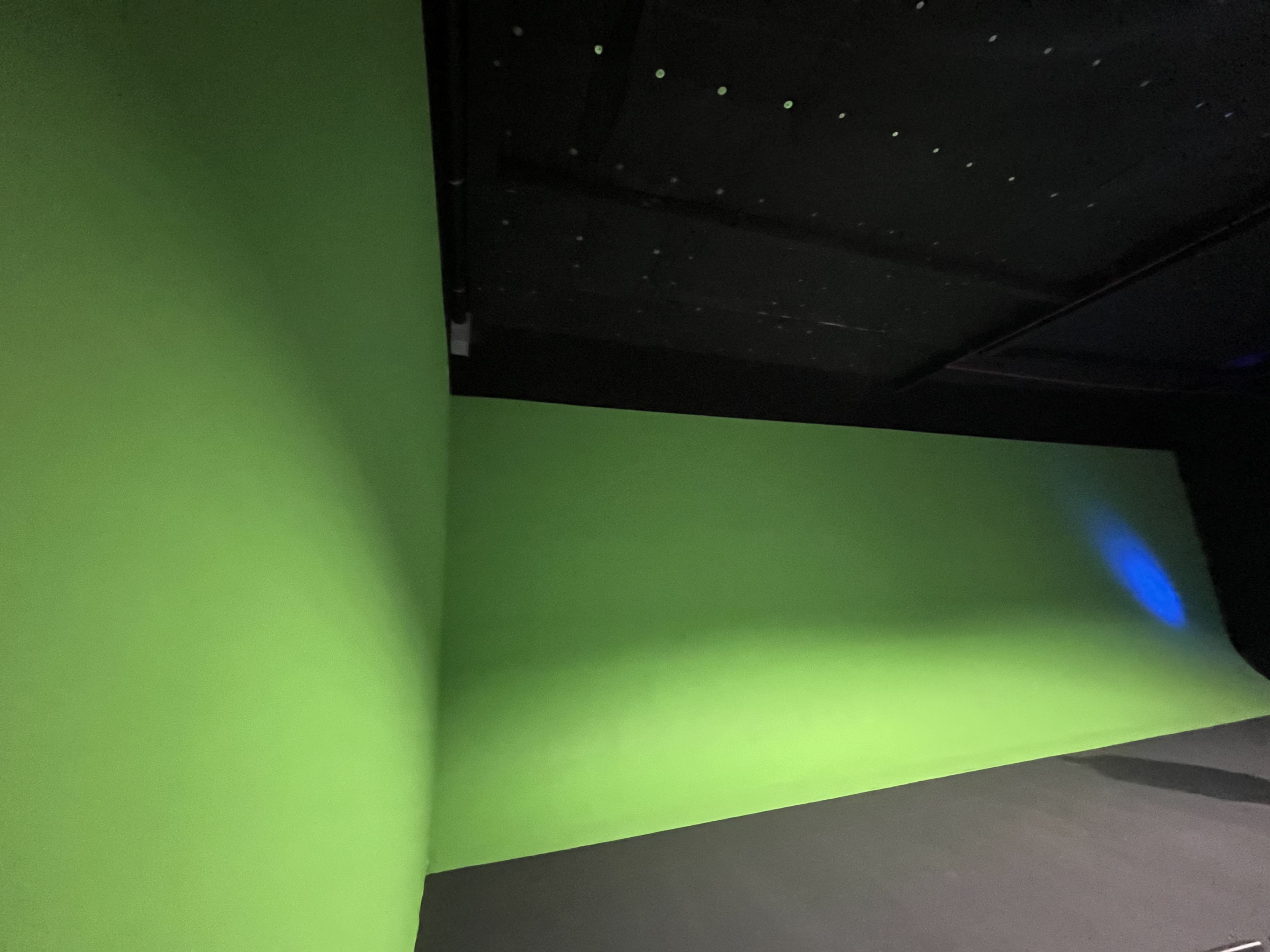 A room with two green walls and a black floor, likely set up for green screen filming.