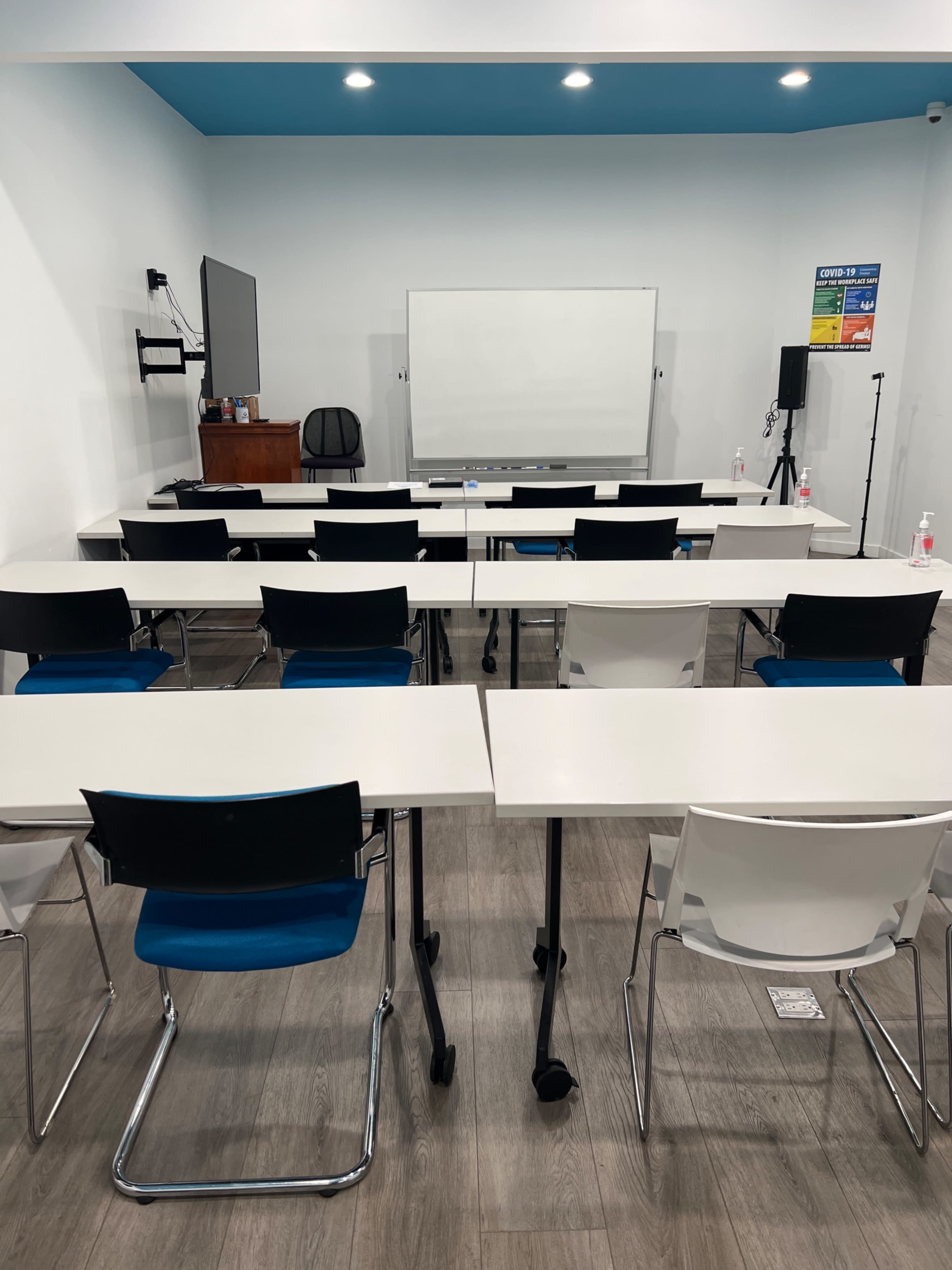A classroom with several rows of tables and chairs, a whiteboard at the front, and a television mounted on the wall.