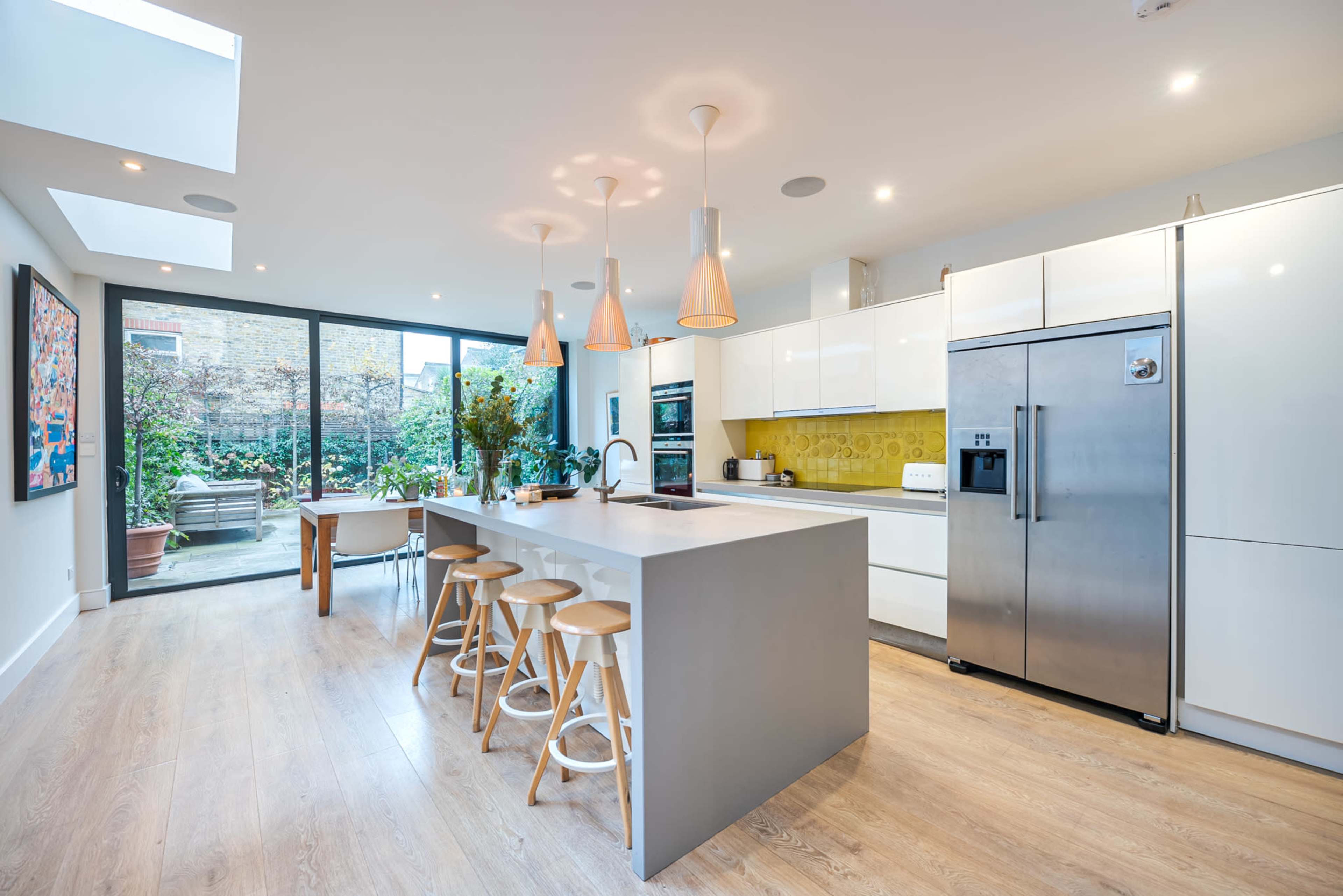 A modern kitchen features a large island with stools, stainless steel appliances, and large glass doors leading to an outdoor space.