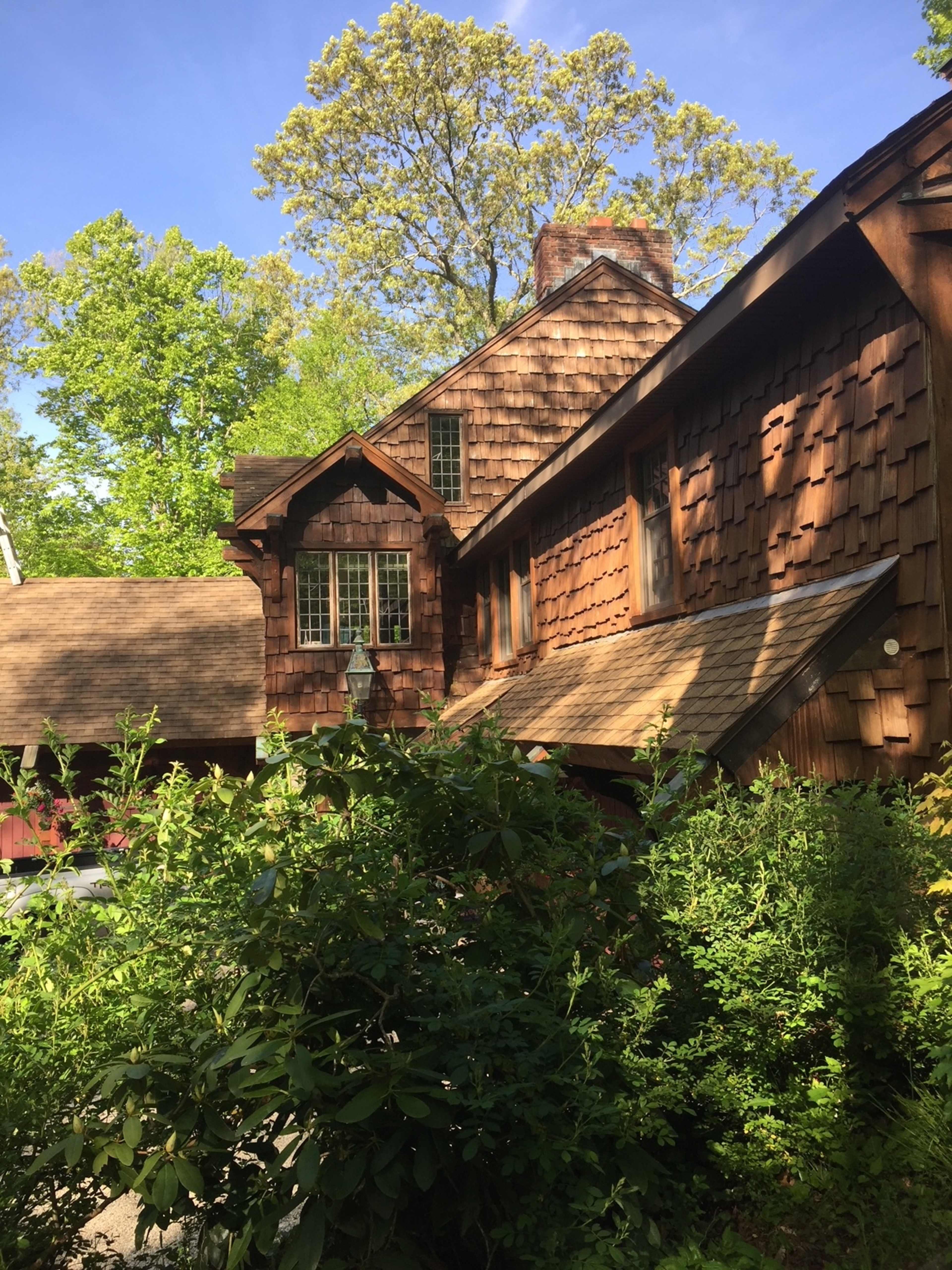 A wooden house with a shingled exterior surrounded by lush greenery and trees.