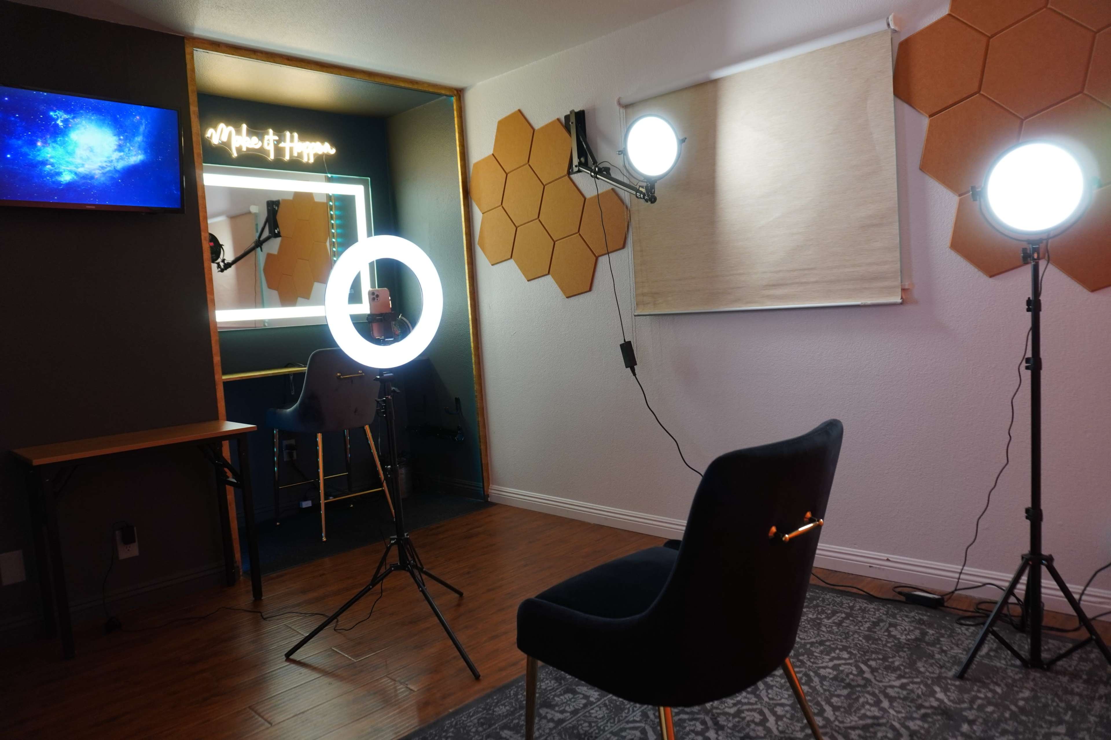 A well-lit studio space featuring a chair, a ring light, two additional lights, and a decorative wall with hexagonal panels.