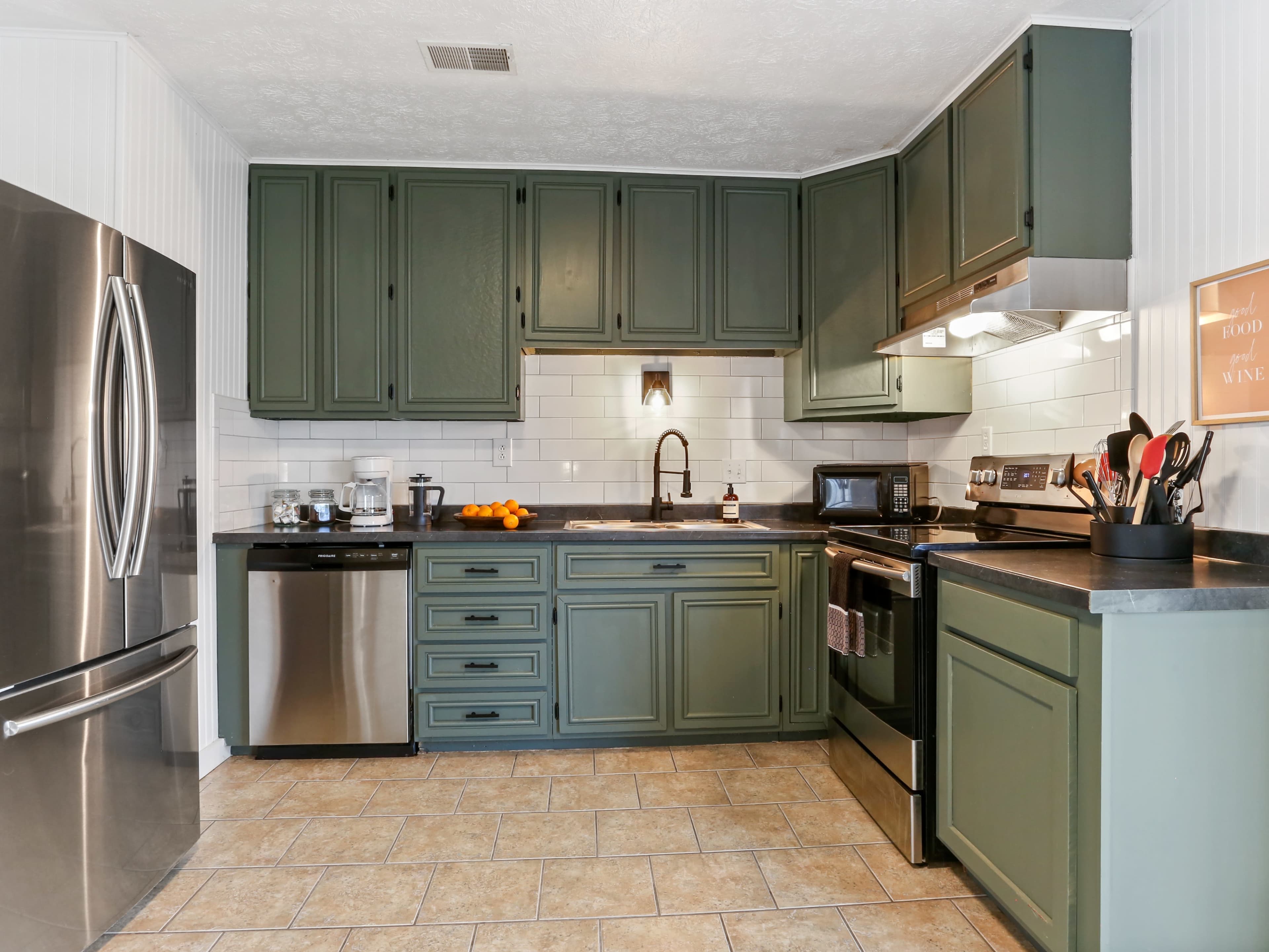 The kitchen features green cabinetry, stainless steel appliances, and a tile floor.