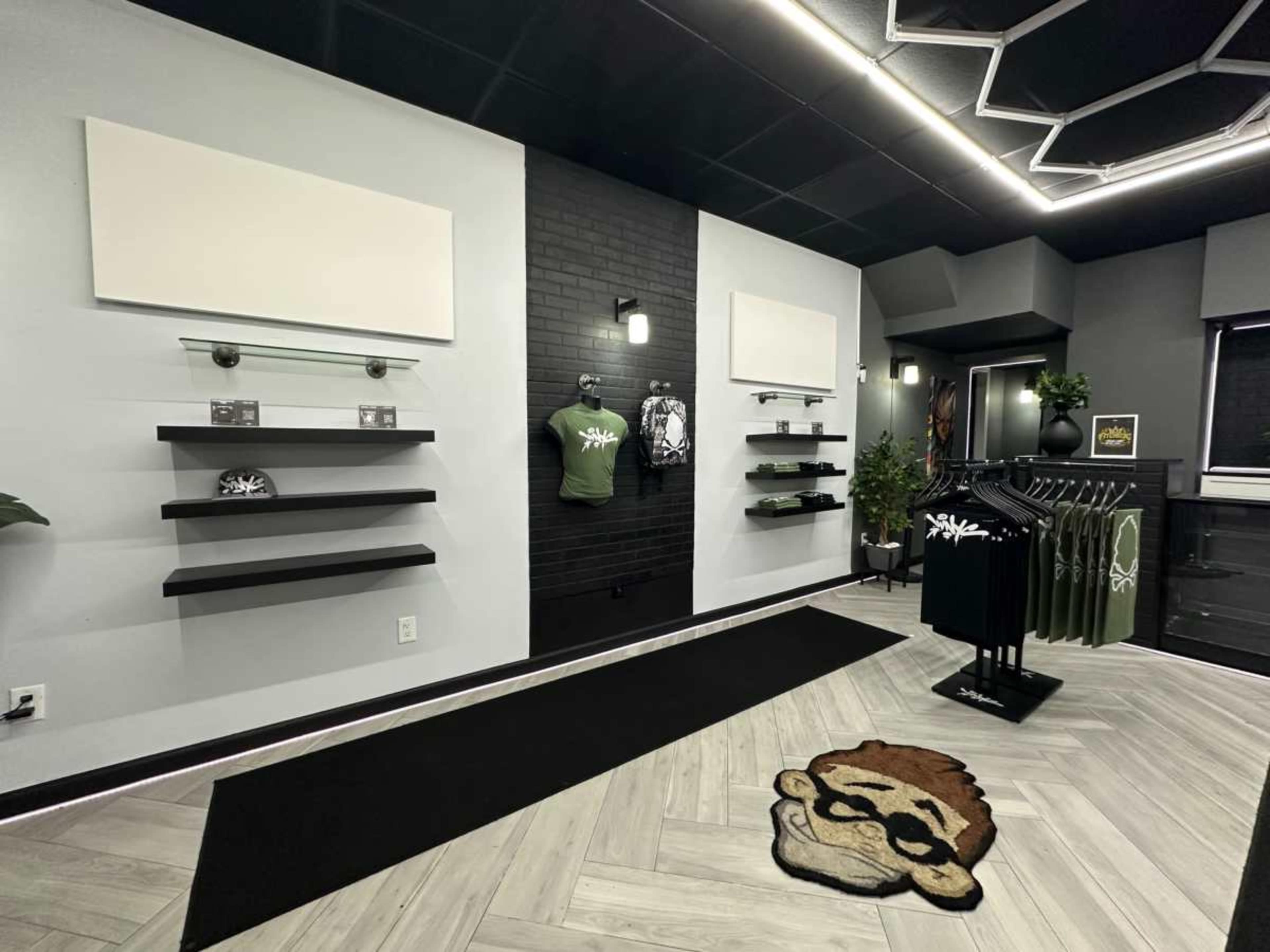 The image shows a modern retail space featuring gray walls, black accents, empty display shelves, and clothing racks with various apparel items.