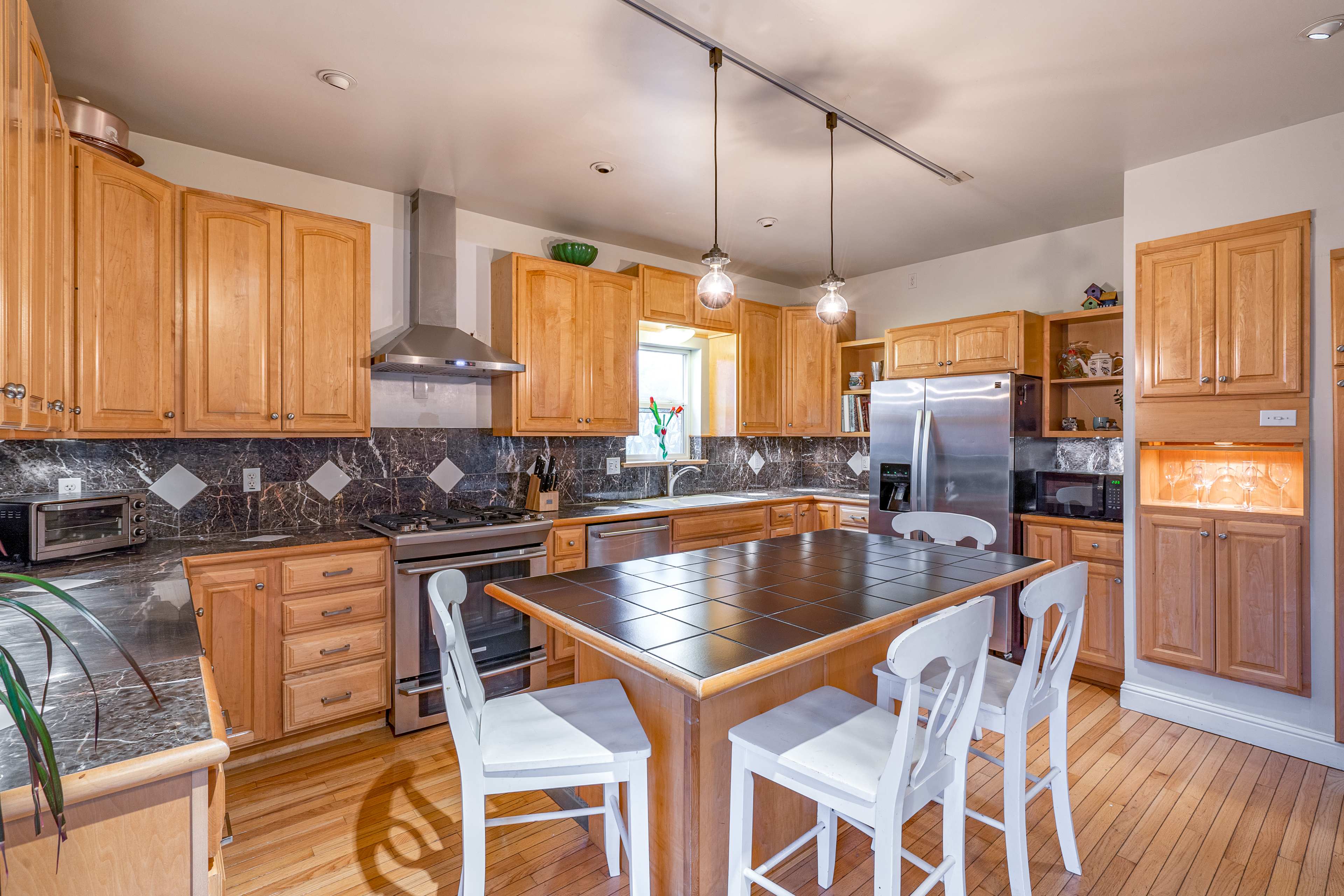 A modern kitchen features wooden cabinets, a central island with seating, stainless steel appliances, and a marble backsplash.