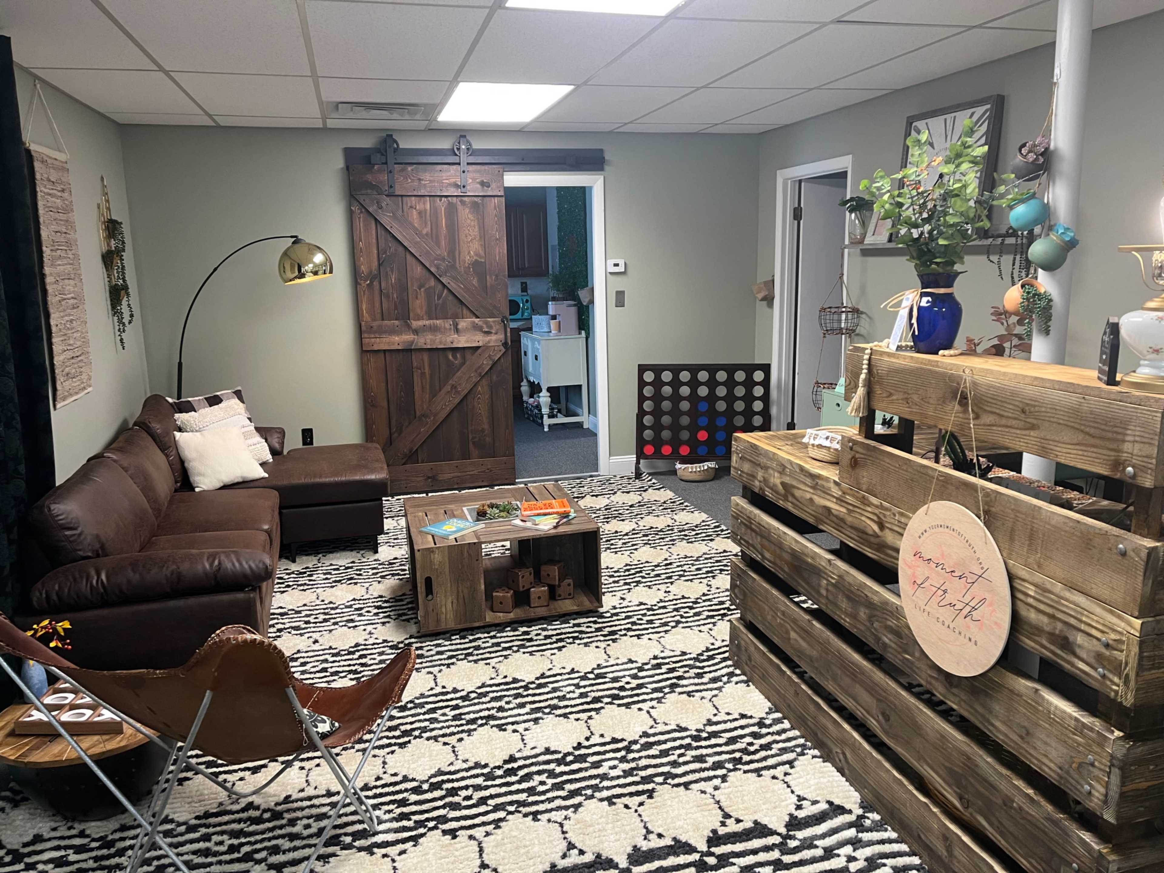 The image shows a cozy basement living area with a brown leather couch, a decorative wooden coffee table, and a wooden partition with various decorative items.