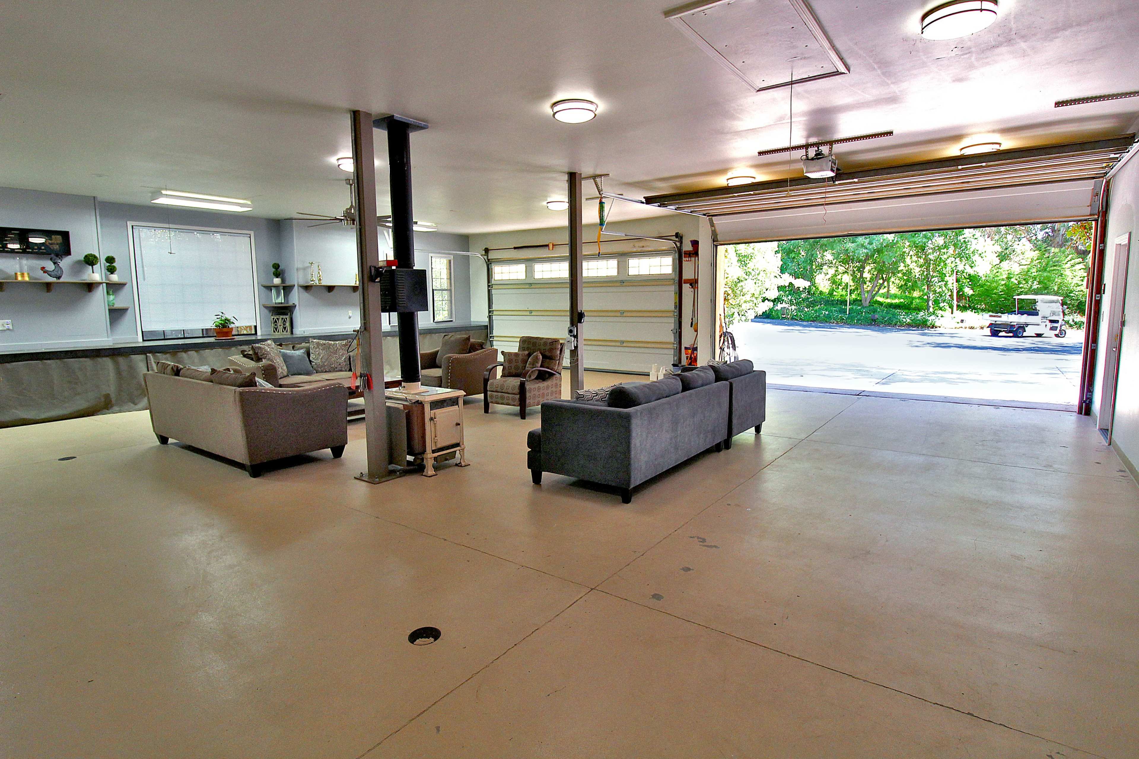 A spacious garage with two sofas arranged around a small table, and a large open garage door revealing a view of the outdoors.