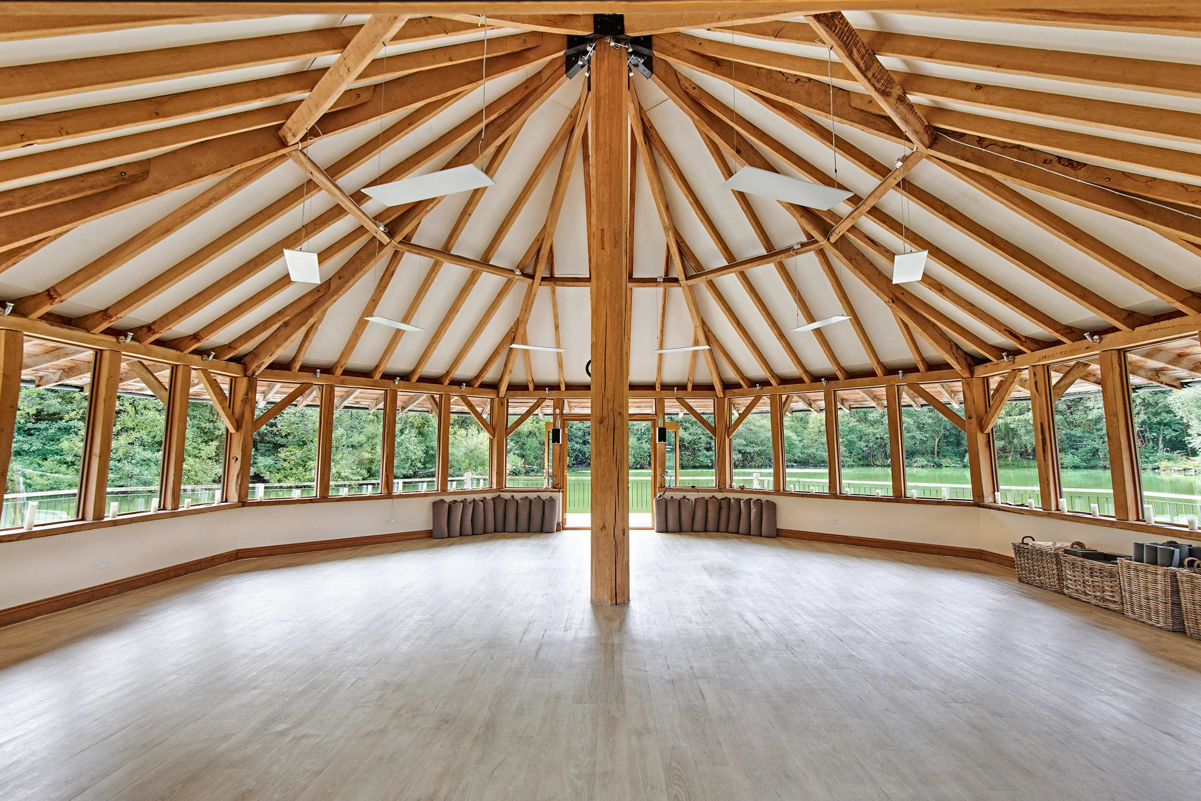 The interior of a circular wooden structure features exposed beams and large windows overlooking a green landscape.