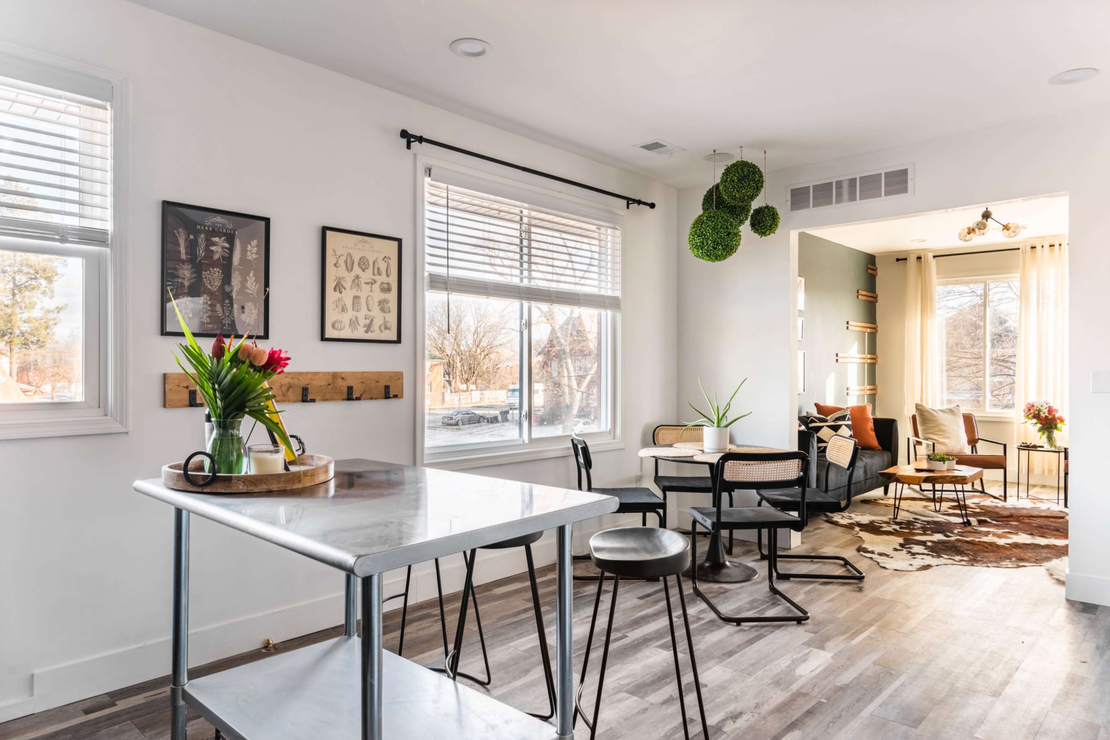 A modern, open-layout living area features a dining table with chairs, a kitchen island, and a seating area with a couch and shelves.